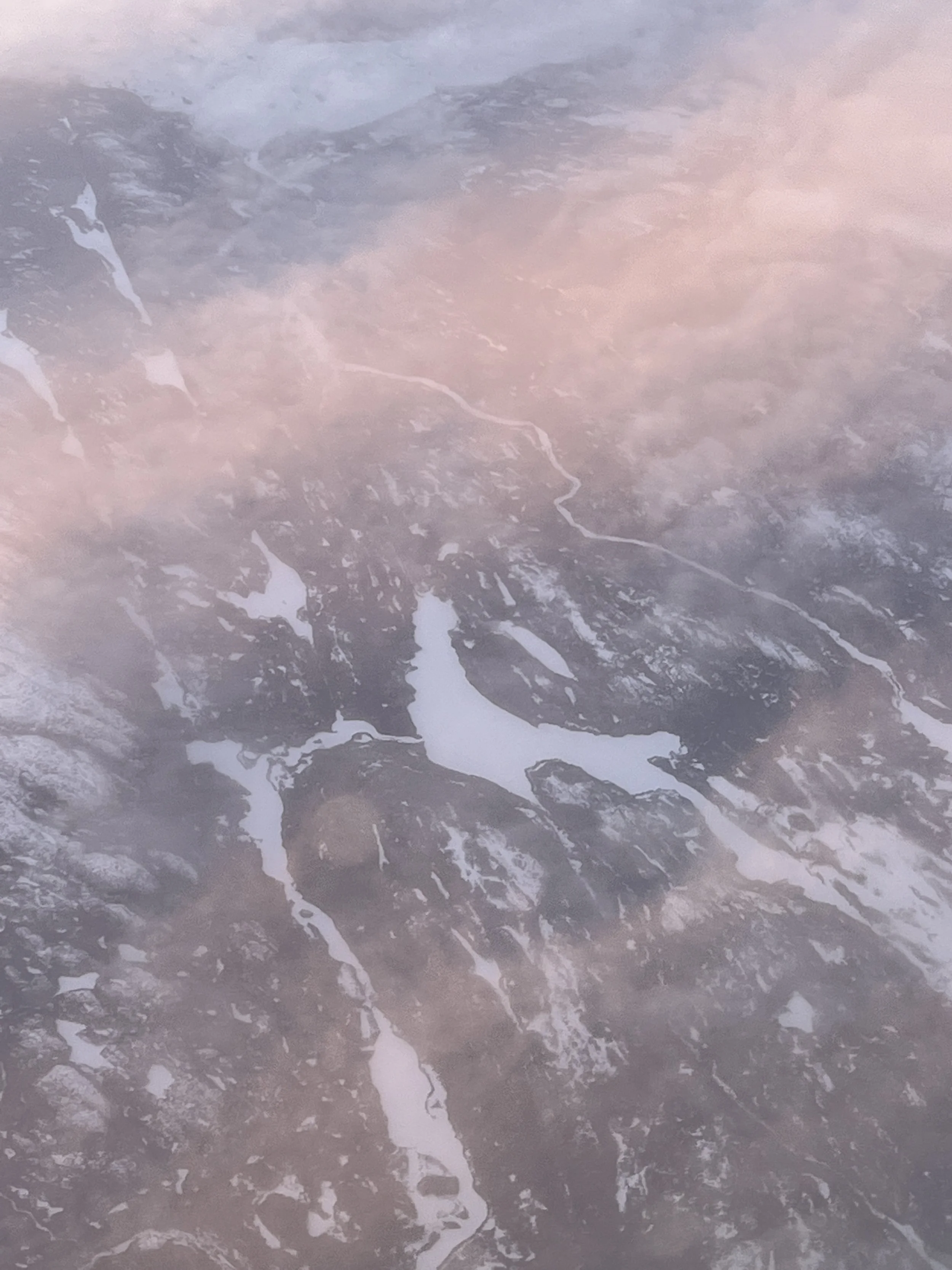 Aerial view of a river winding through snow-capped mountains during sunset, with pink and purple hues in the sky.