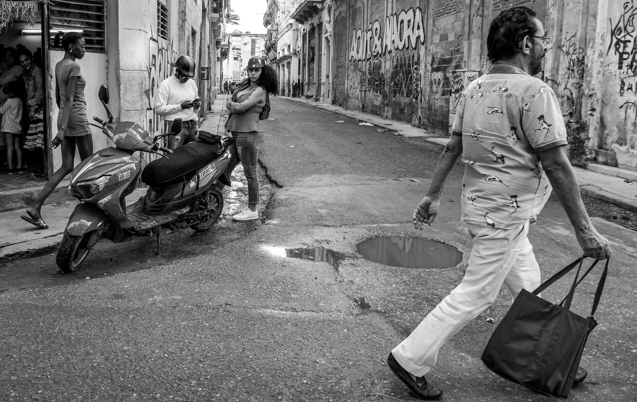 Street scene in a city with pedestrians, a motorbike, and graffiti on the walls, in black and white.