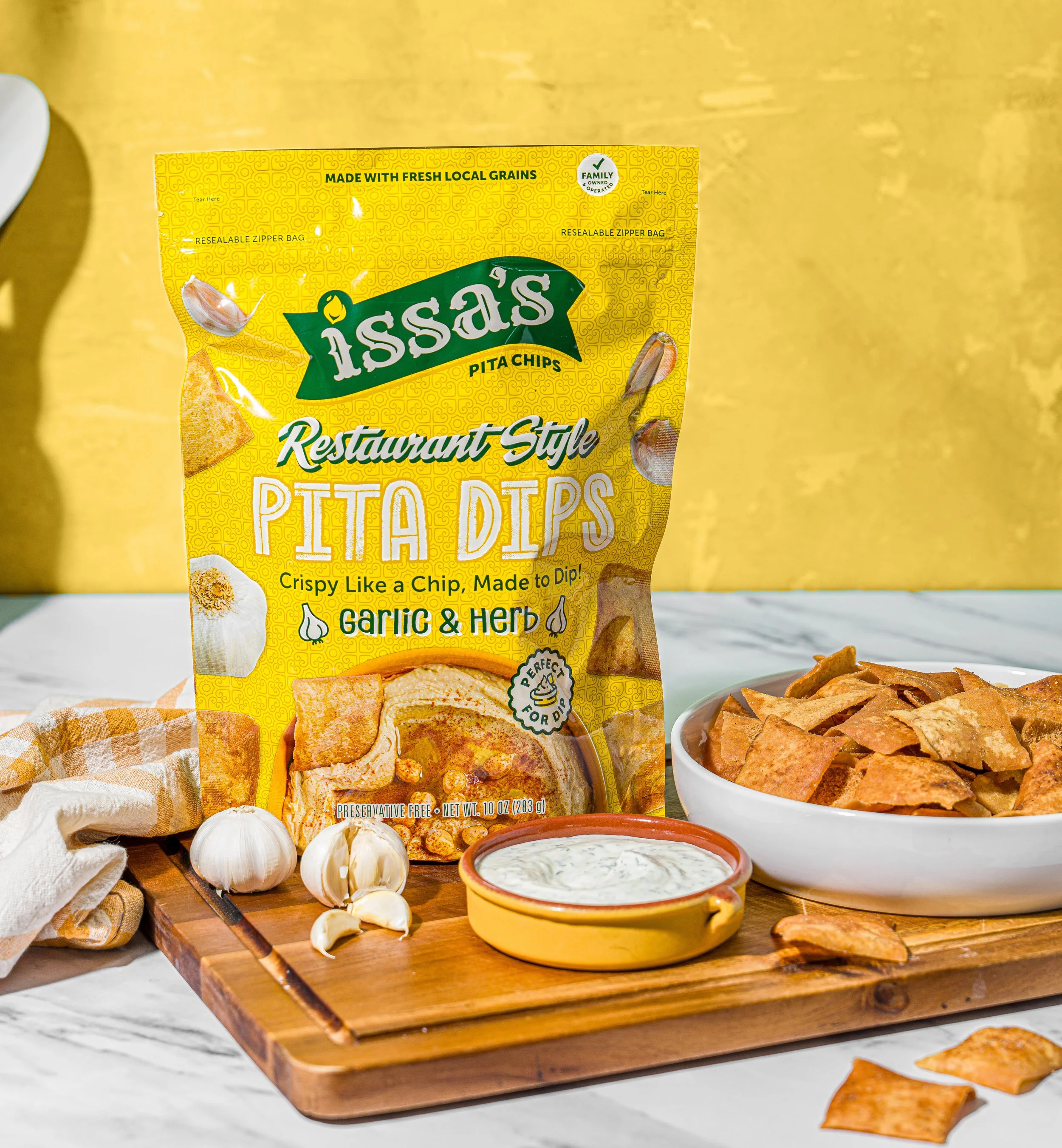 Issa’s Restaurant Style Garlic & Herb Chips, 10 oz bag with dip on a board.
