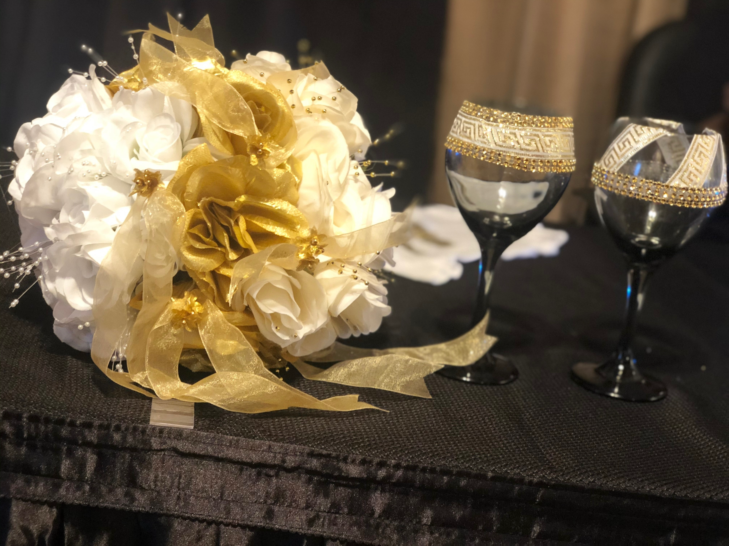 A custom-designed bridal set featuring a handcrafted white and gold bouquet and matching his-and-her wine glasses with elegant African-inspired gold trim — designed by Moments Planning to symbolize unity, heritage, and luxury.