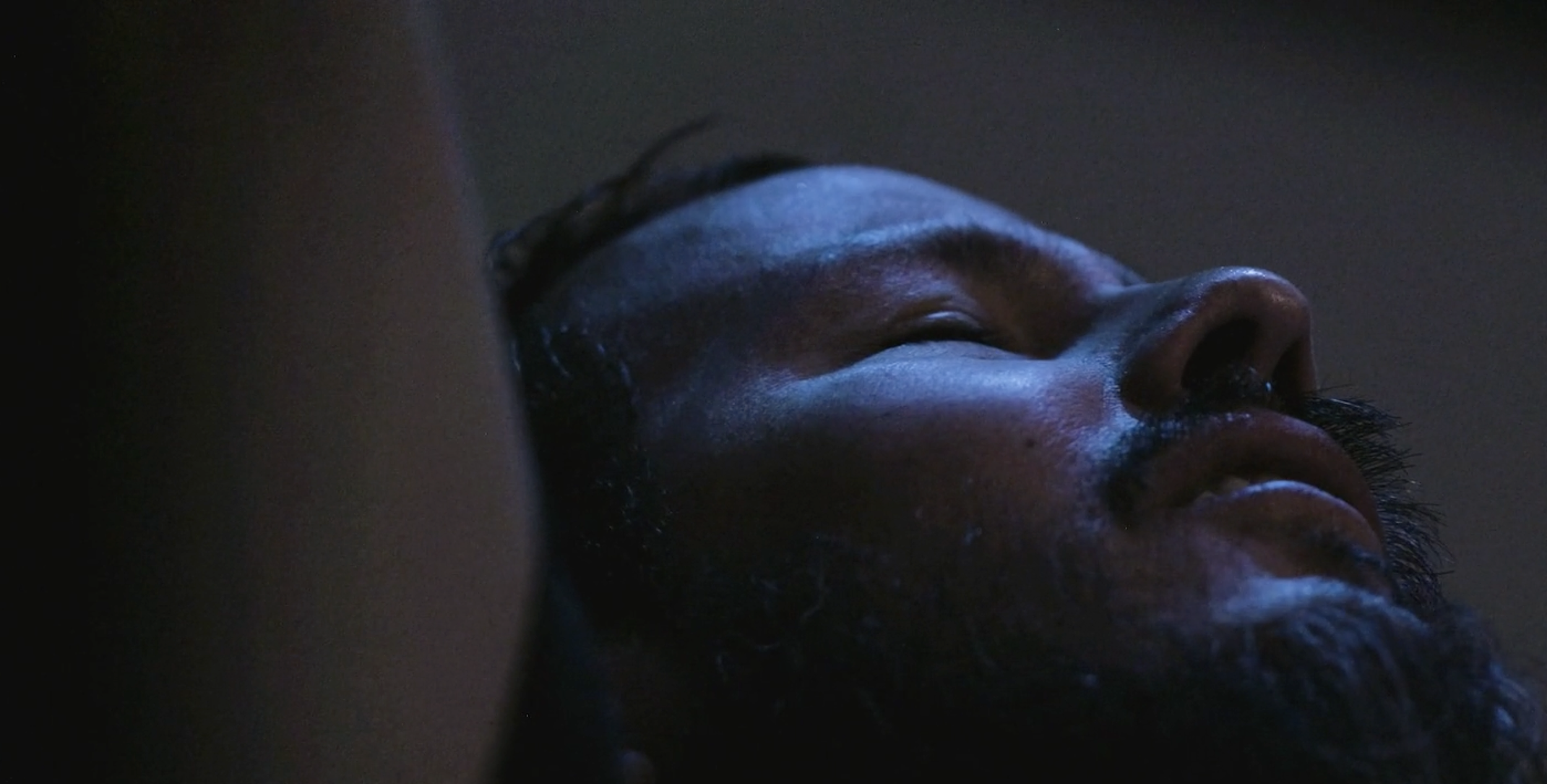 Close-up of a man's face sleeping in low light.