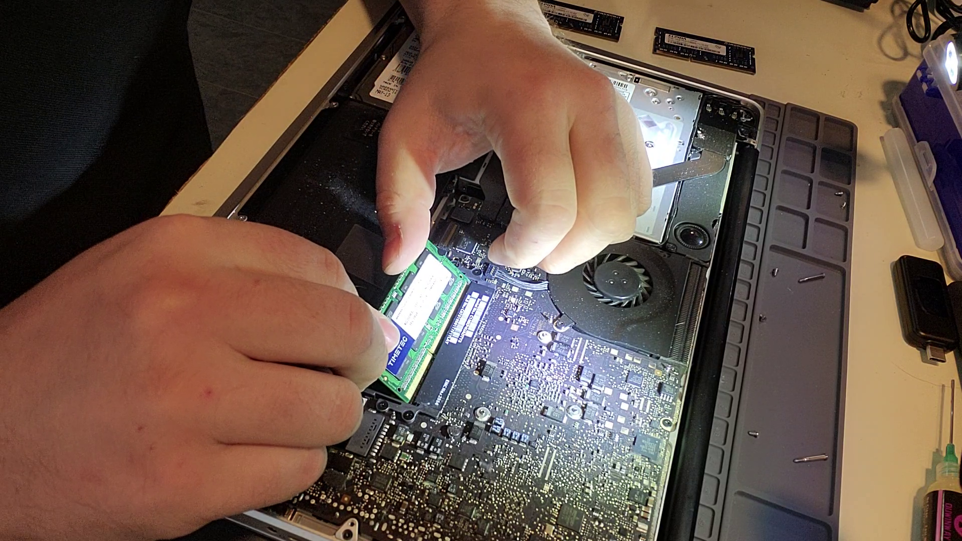 Close-up of hands installing a RAM module into a laptop's motherboard.