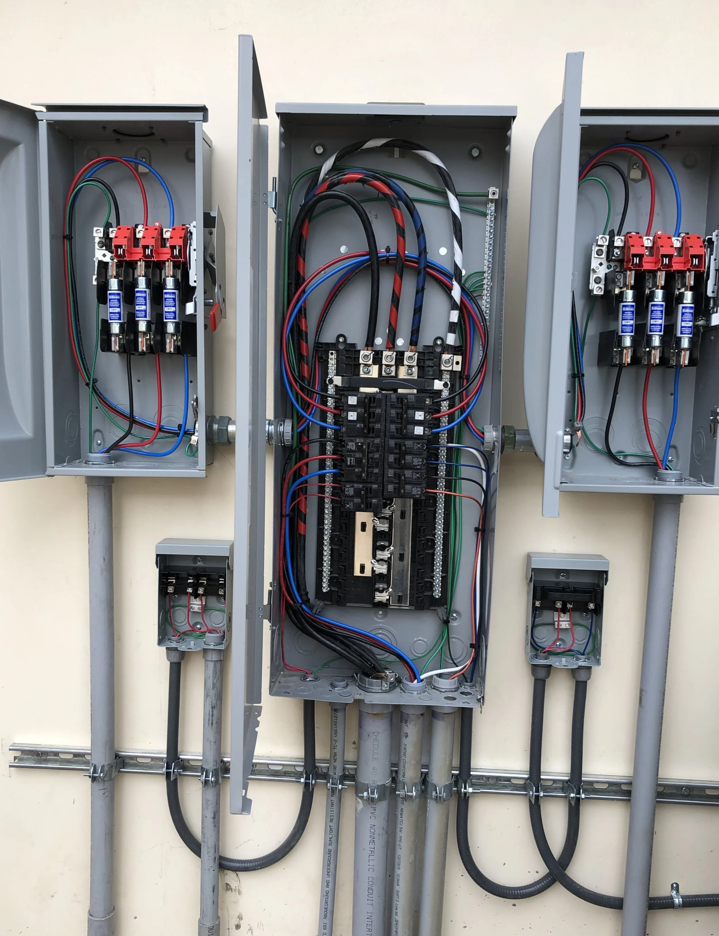 Open electrical breaker box with circuit breakers, wiring, and conduit pipes.
