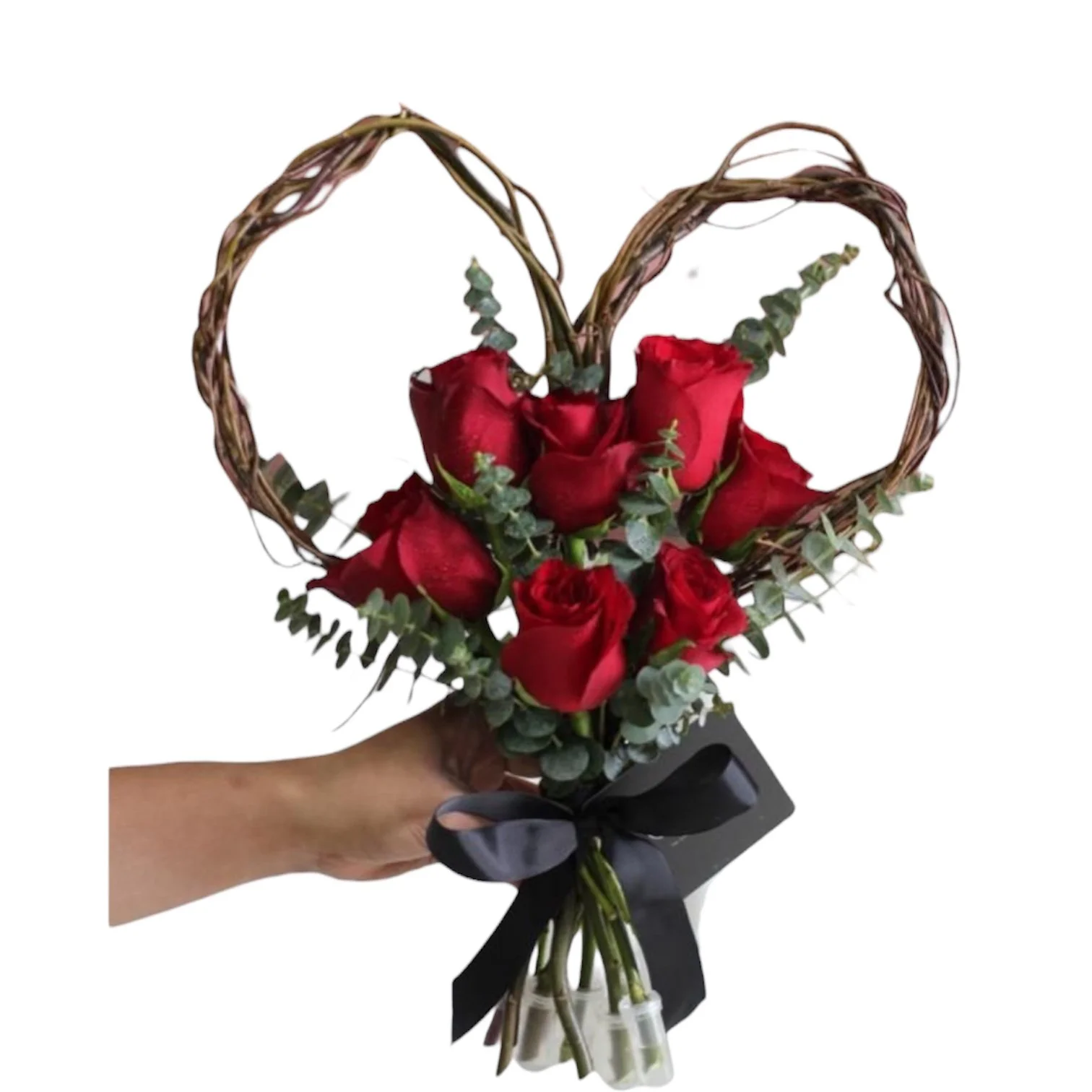 A hand holding a bouquet of red roses with green foliage, accented by a heart-shaped wicker frame and wrapped with a black ribbon.