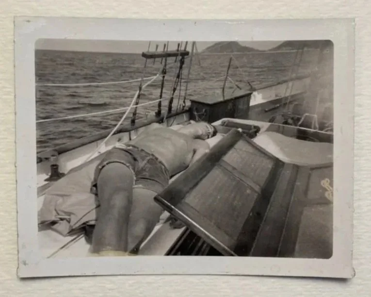A photograph of a man sunbathing on the deck of a sailboat.