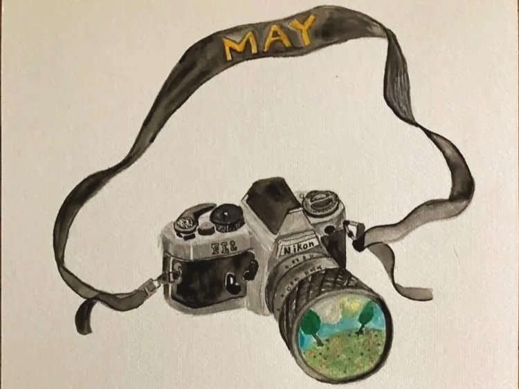 A drawing of a vintage Nikon camera with a lens showing a landscape with trees and grass. The camera strap spells out "MAY" in yellow letters.