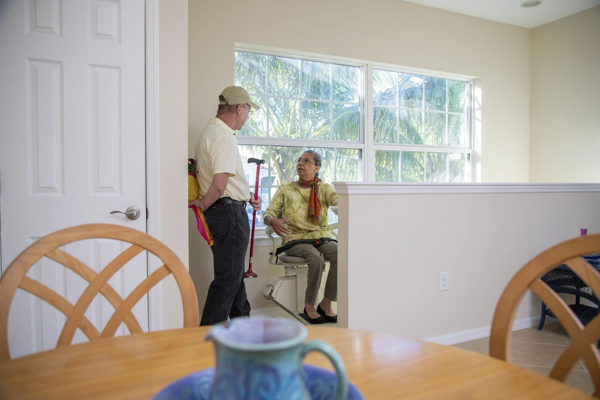 Man with baseball cap holding cane for elderly senior using stairlift.