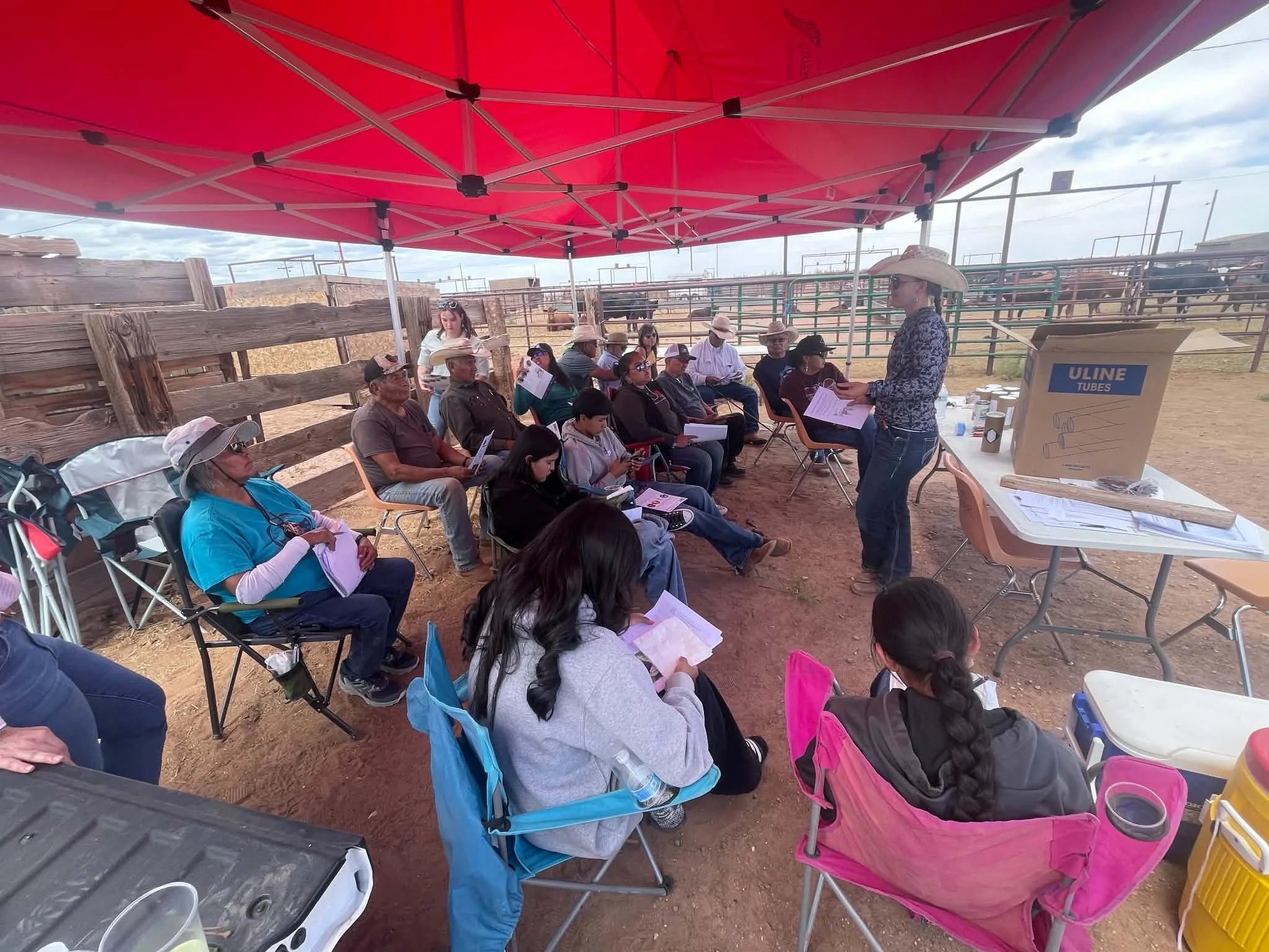 veterinarian wearing cowboy hat speaking to crowd of ranchers under a red tent