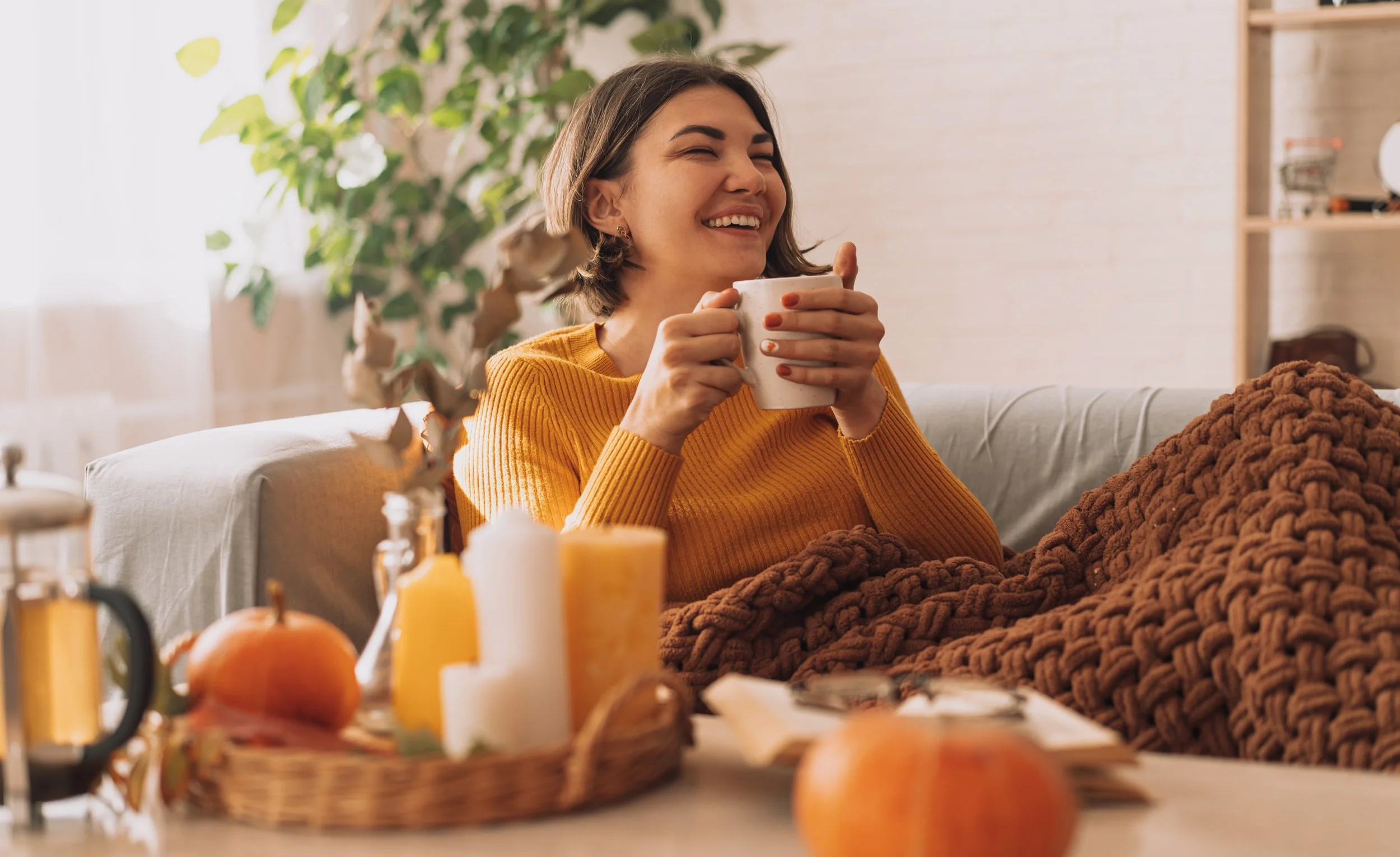 Smiling woman relaxing with a warm drink in a cozy, sunlit room during fall.