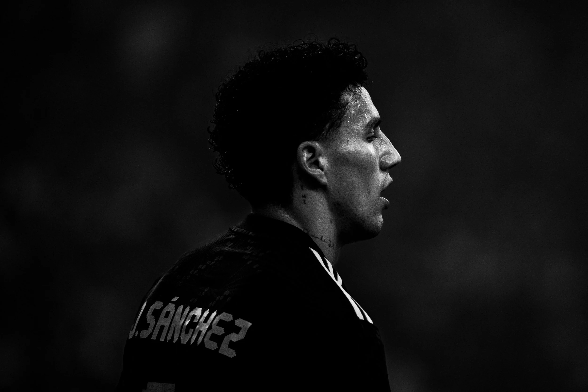 Black and white profile photo of a male athlete with curly hair, wearing a sports jersey with the name 'SÁNCHEZ' visible on the back.