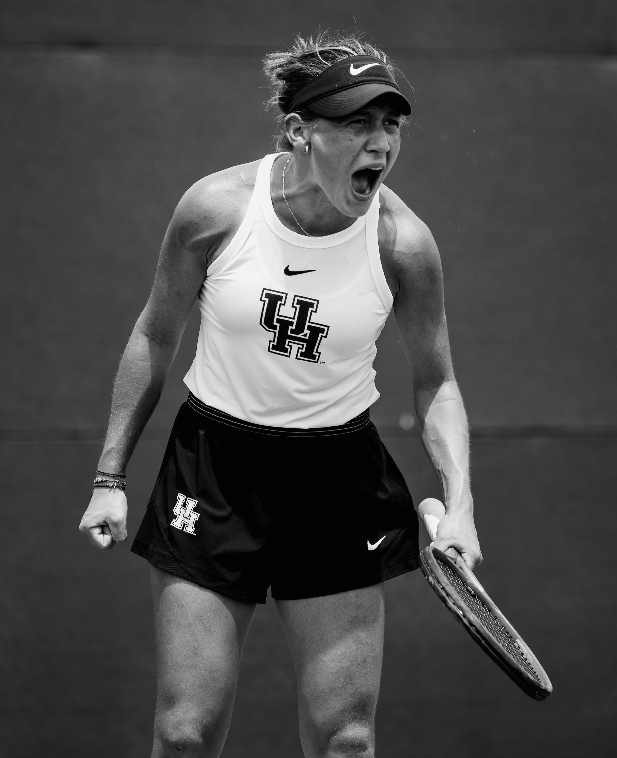 A female tennis player, wearing a University of Houston athletic uniform, is expressing intense emotion on the court.