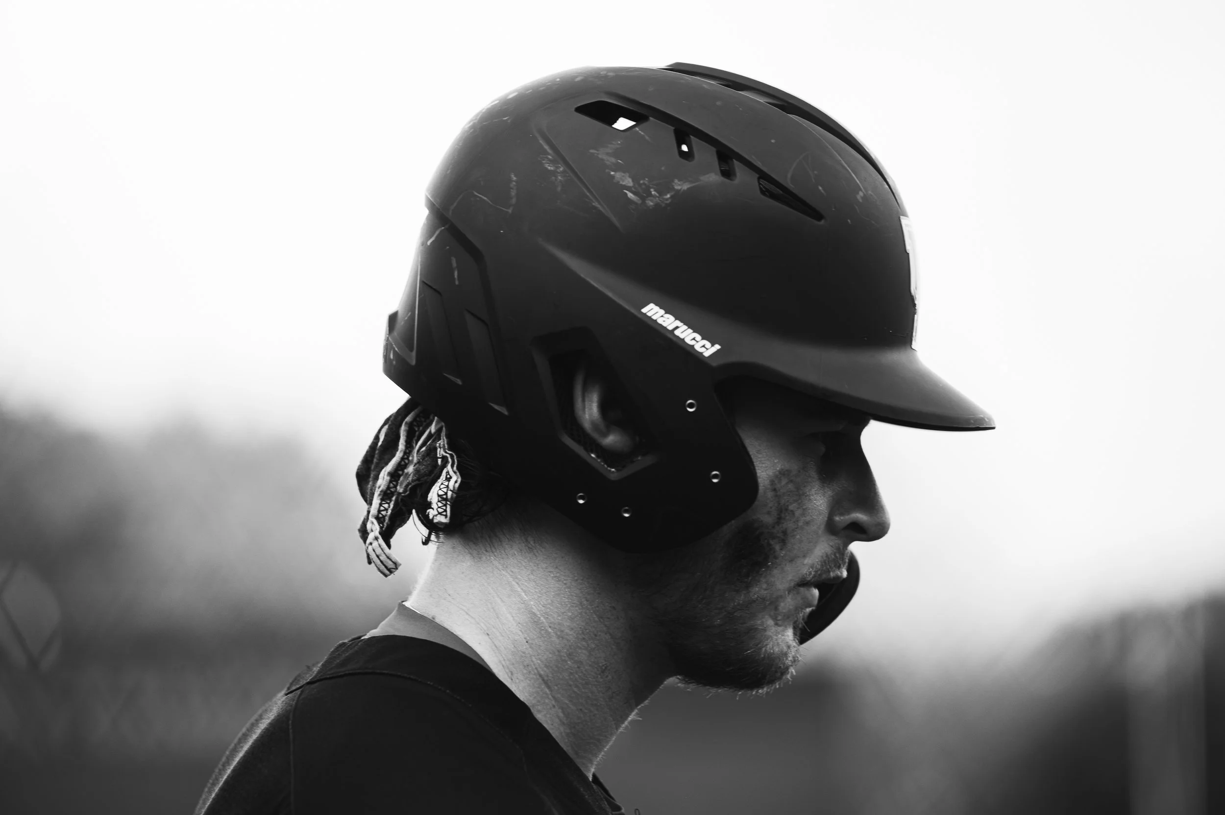 A person wearing a black MARUCCI helmet and a dark shirt, facing right, outdoors with blurred background.