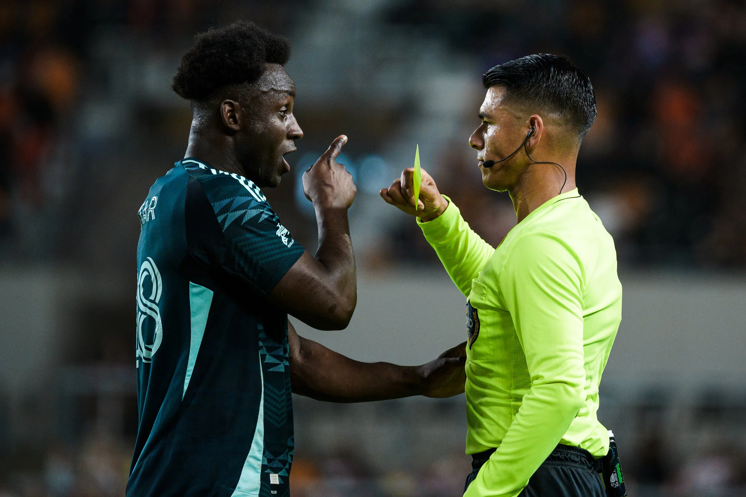 A soccer player in a dark uniform arguing with a referee in a neon yellow shirt during a game.