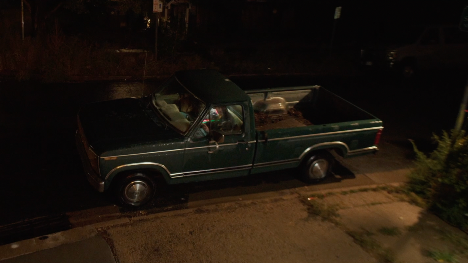 A dark green pickup truck parked on a street at night, seen from an elevated angle, with a person visible inside.