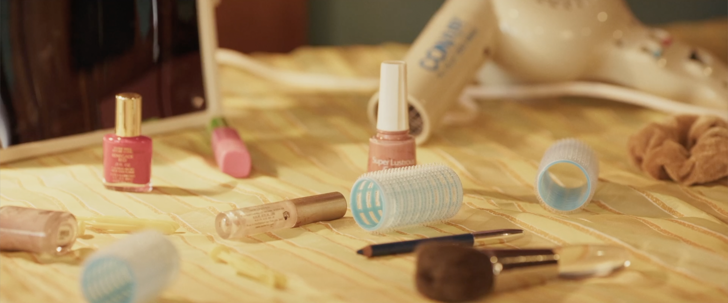 Nail polish bottles, hair rollers, and cosmetic tools on a yellow checkered tablecloth