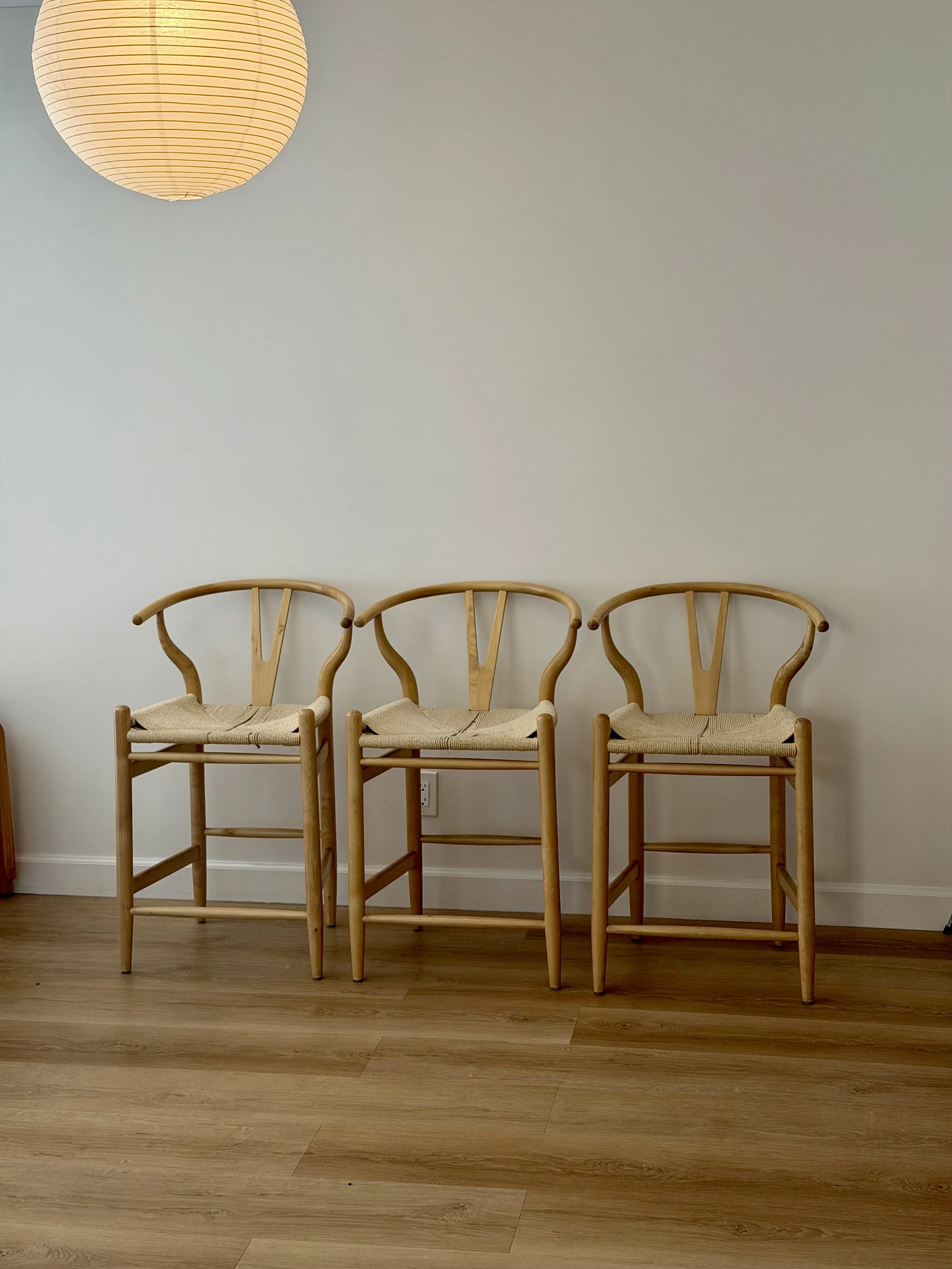 Three wooden chairs with woven seats, positioned against a plain light-colored wall with a paper lantern hanging from the ceiling.