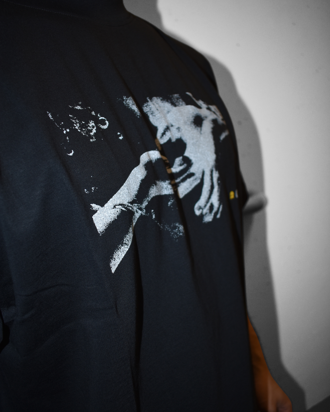 Close-up of a black shirt with a white graphic design of a person's face and hand, partially visible, on a person's chest.