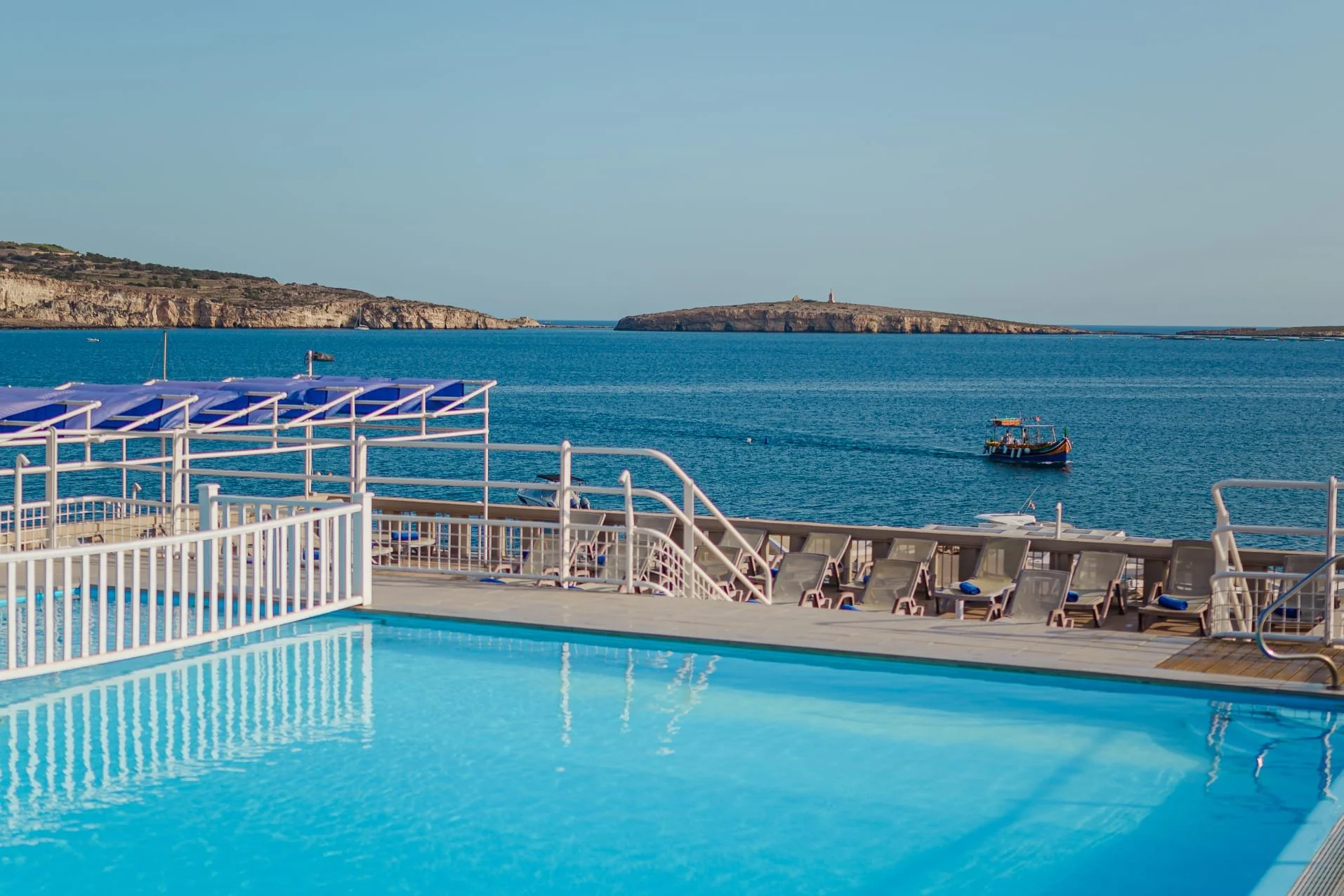 Image of a swimming pool overlooking a large body of water with small boats and an island in the background.
