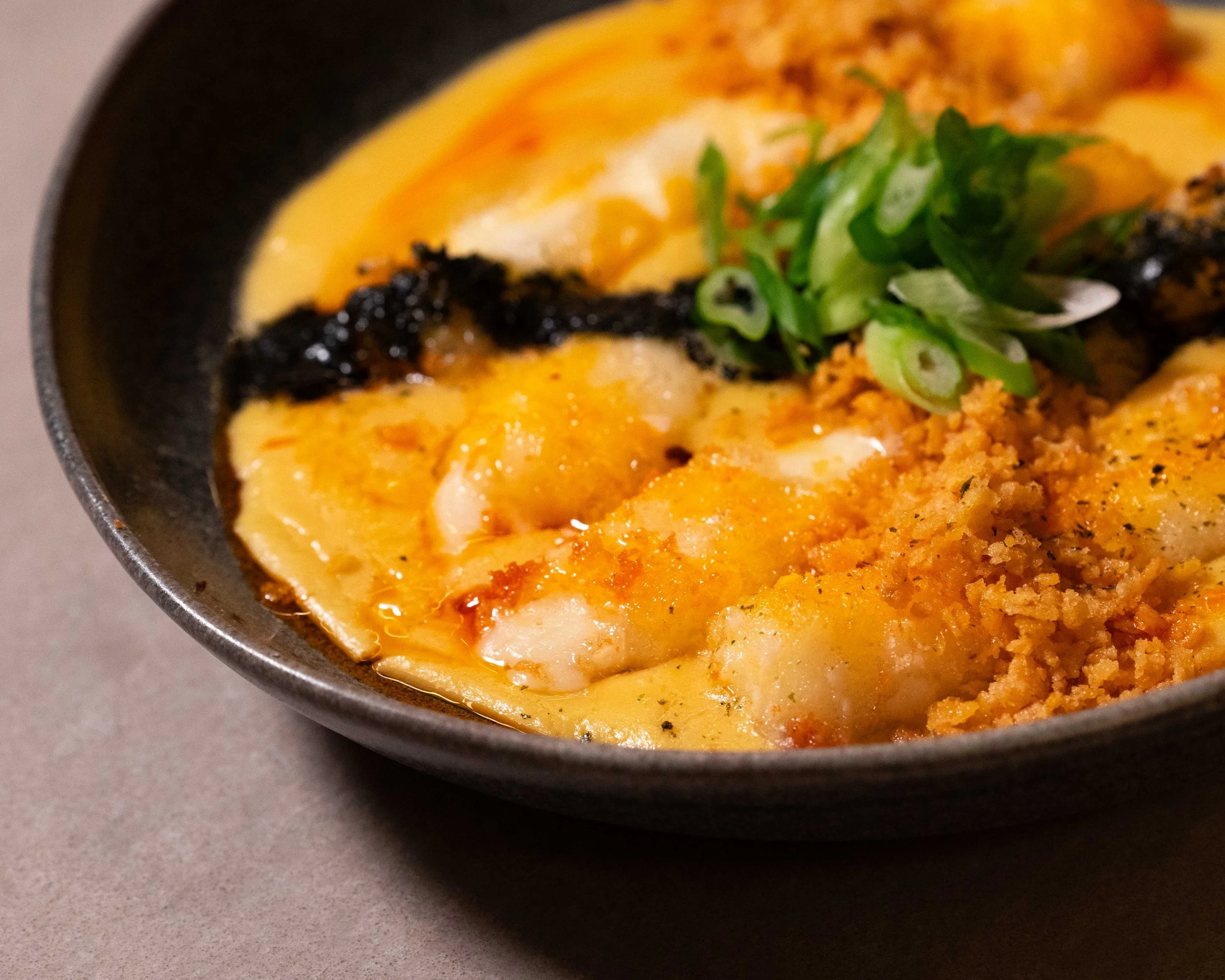 Close-up of a bowl of ramen topped with chopped green onions, black seaweed, and crispy breadcrumbs.