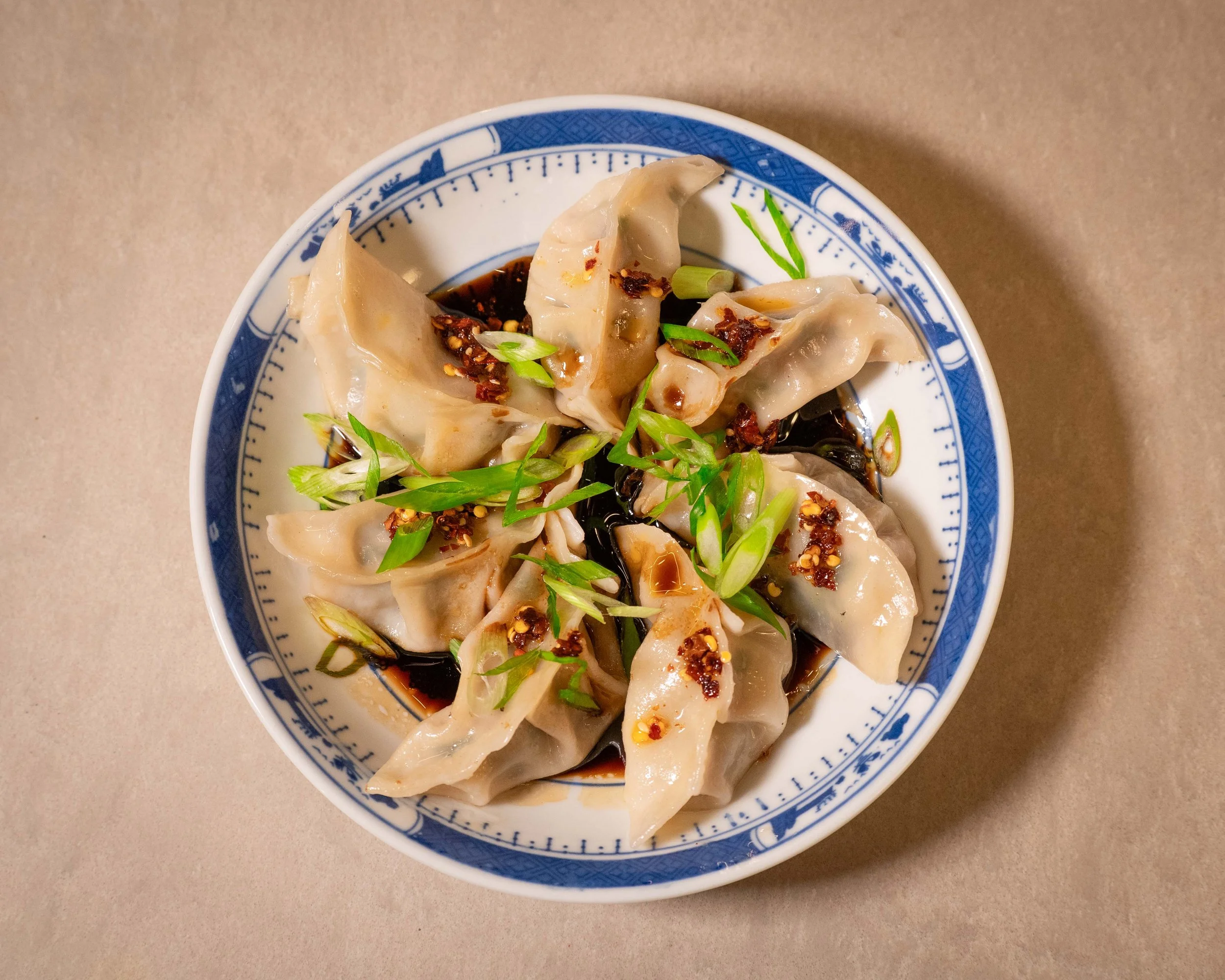 A bowl of Chinese dumplings garnished with chopped green onions and soy sauce with chili flakes.