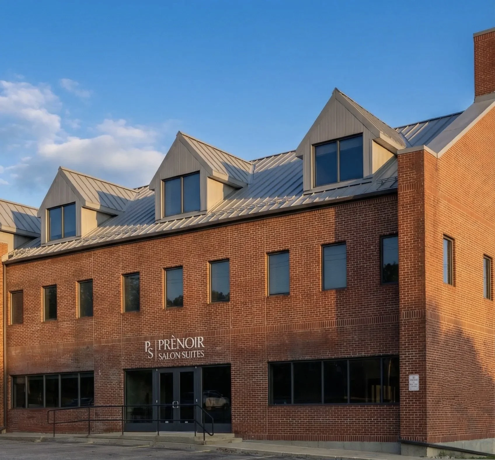 Brick building with windows on the top and bottom floors and a sign with white lettering that says "Prenoir Salon Suites" written on the facade.