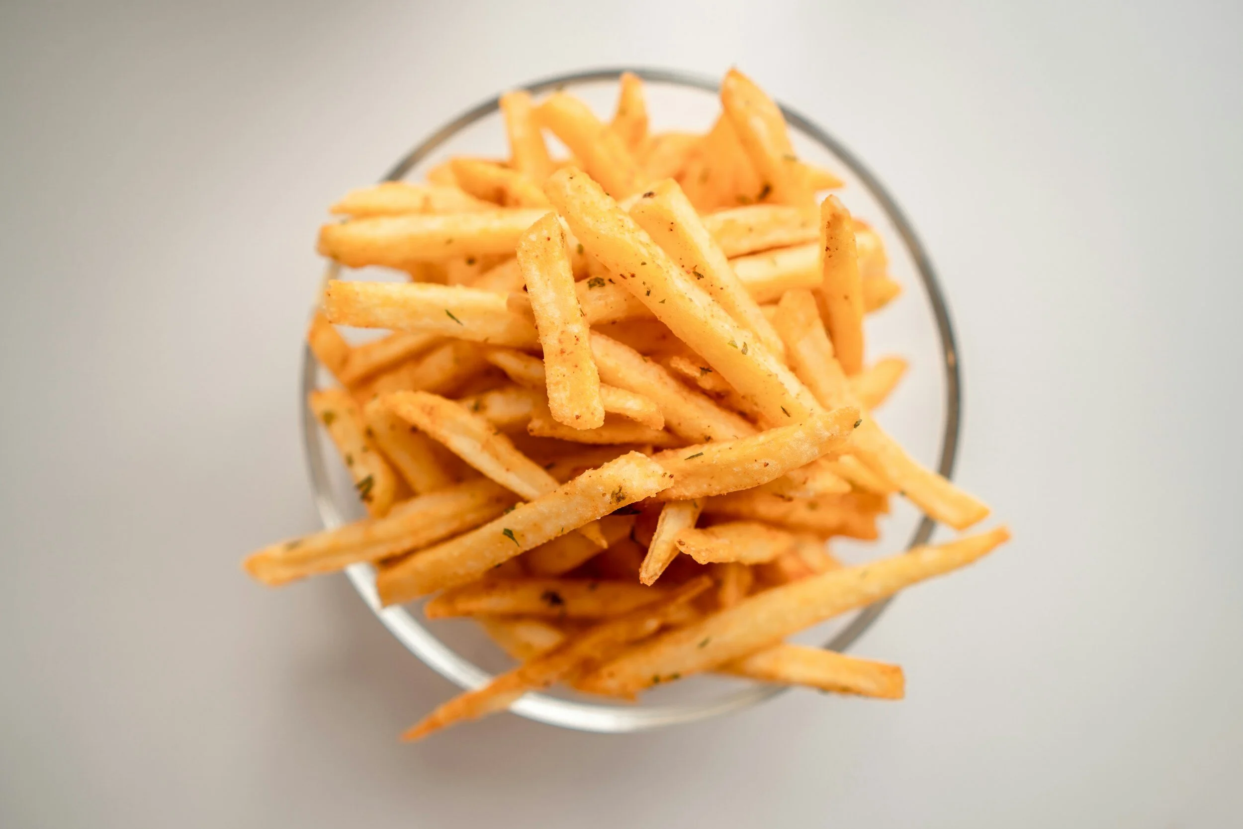 Bowl of seasoned French fries on a white background.