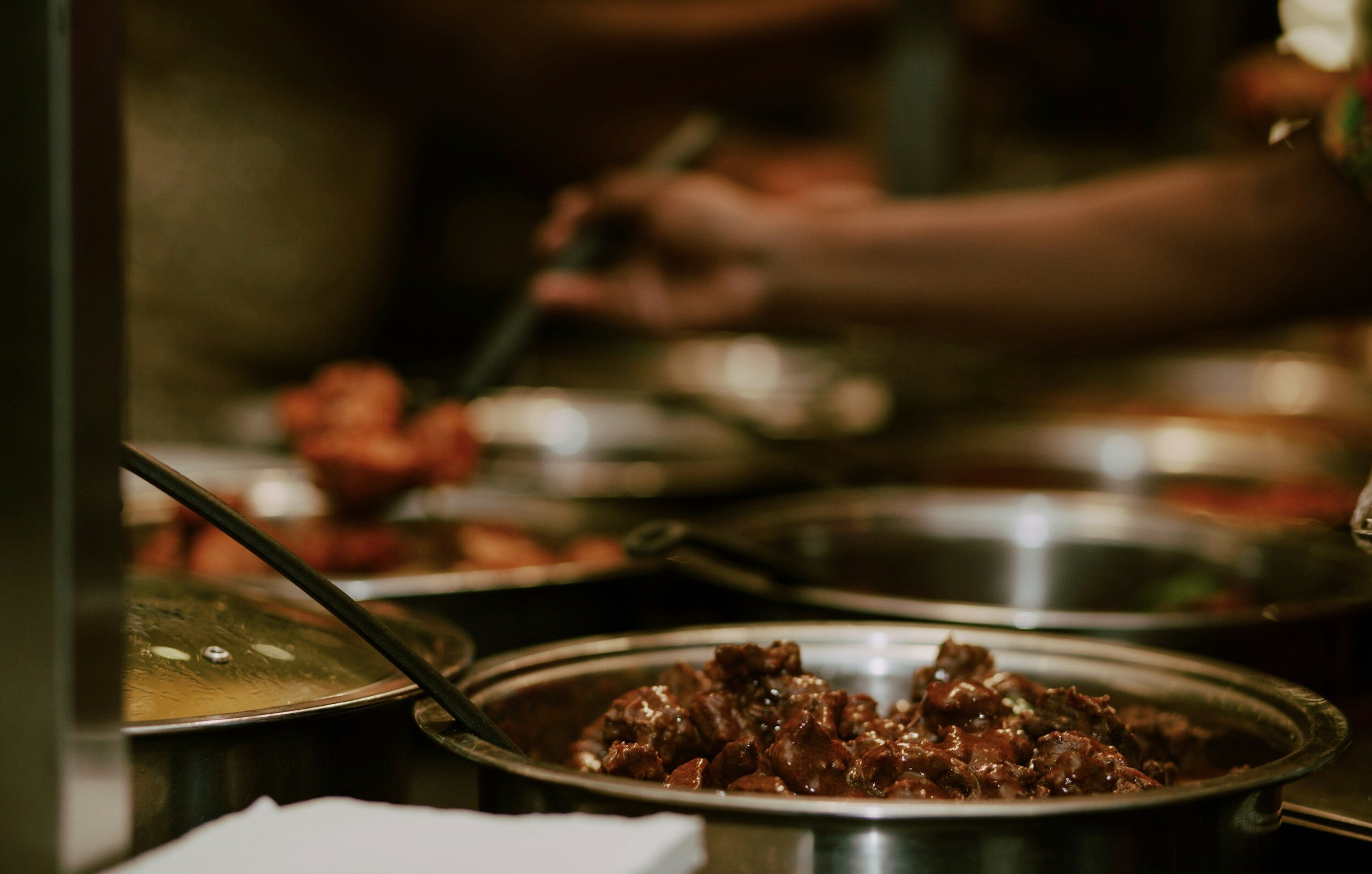 Close-up of a buffet with trays of cooked food, including meat dishes.