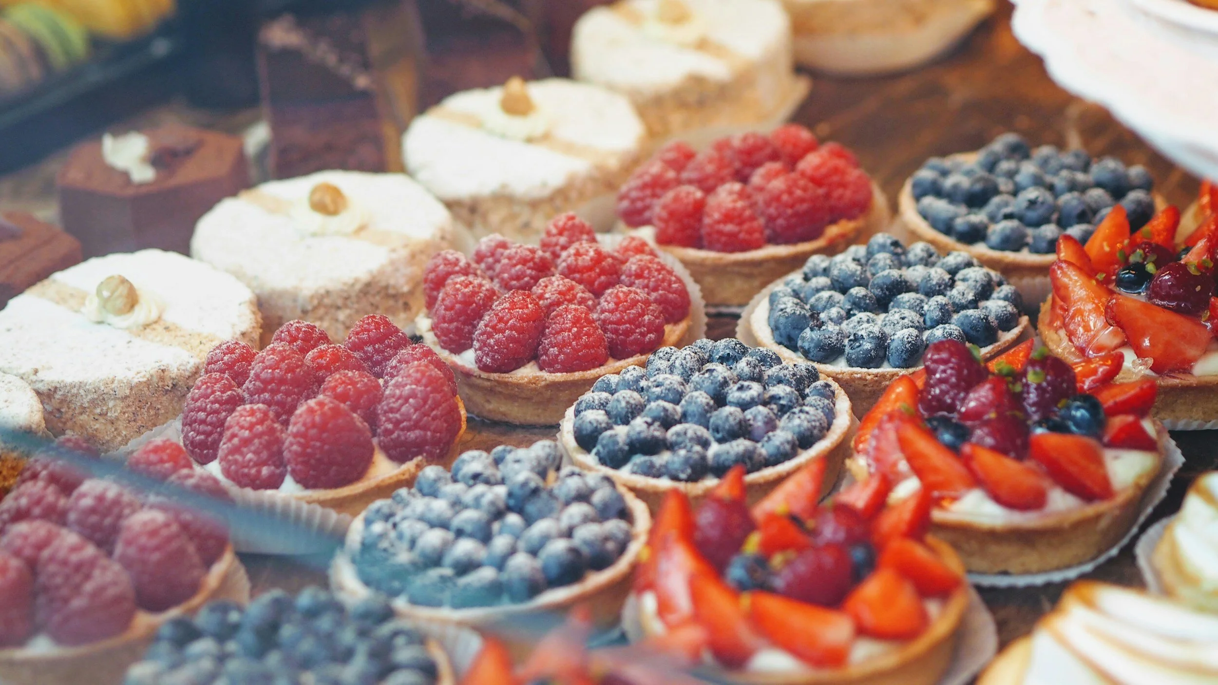 Assorted fruit tarts with raspberries, blueberries, and strawberries in a bakery display.