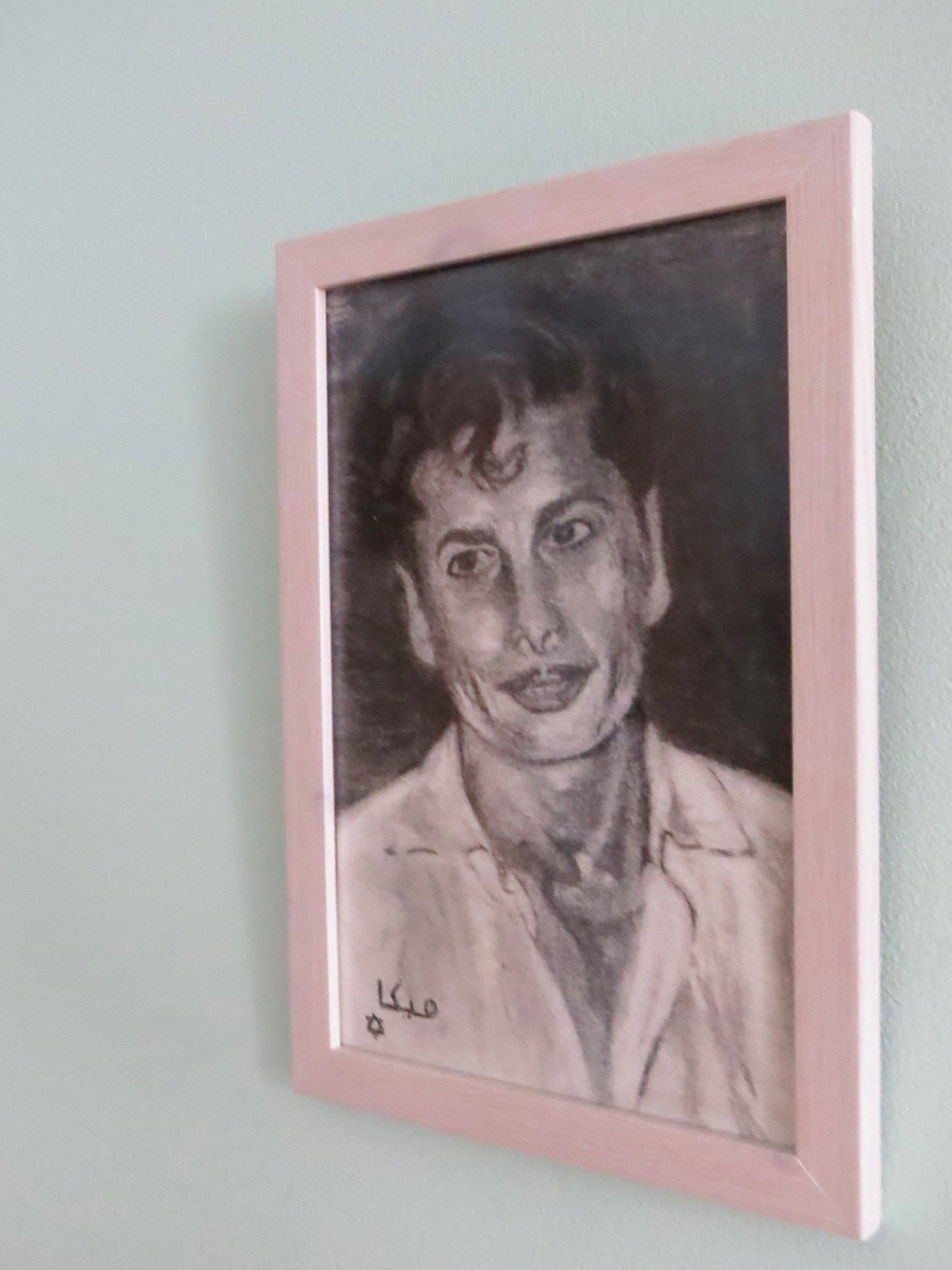 A framed black-and-white portrait drawing of a woman with short hair, wearing a collared shirt, hanging on a light-colored wall.