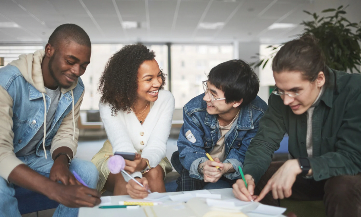Five young adults sitting together and working on a project in a modern office space, smiling and engaging with each other.