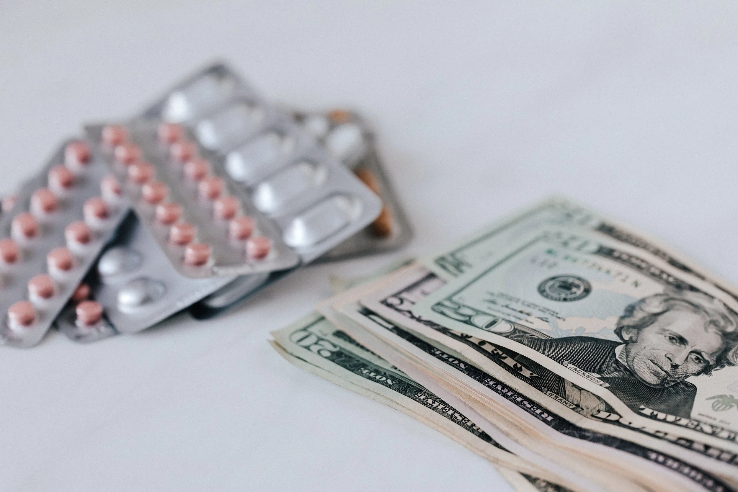 HEalthcare affordability. Prescription affordability. Medicare. Medicaid. Social Security. Blister pack of pink pills, some tablets are missing, placed on top of a stack of US 50-dollar bills.
