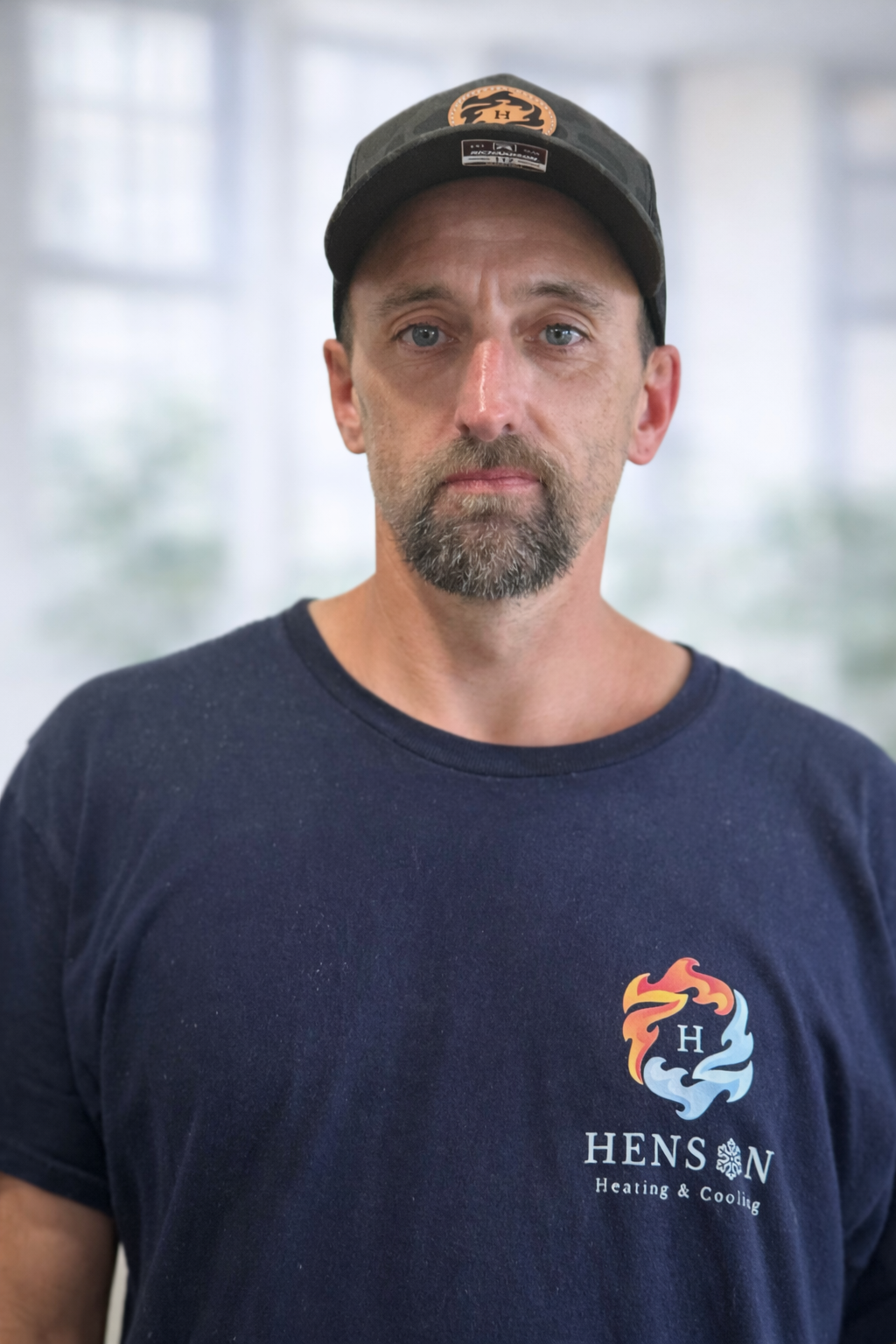 Man wearing a black cap and navy blue t-shirt with Hens on Heating & Cooling logo, standing against a plain background.