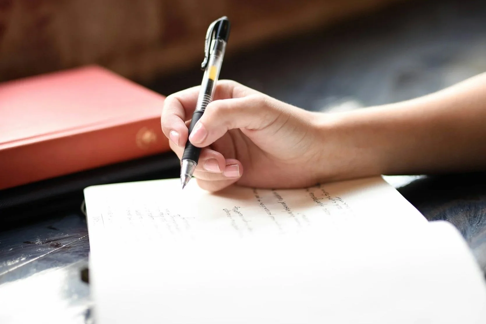 Woman’s hand writing in a journal on a soft wooden table