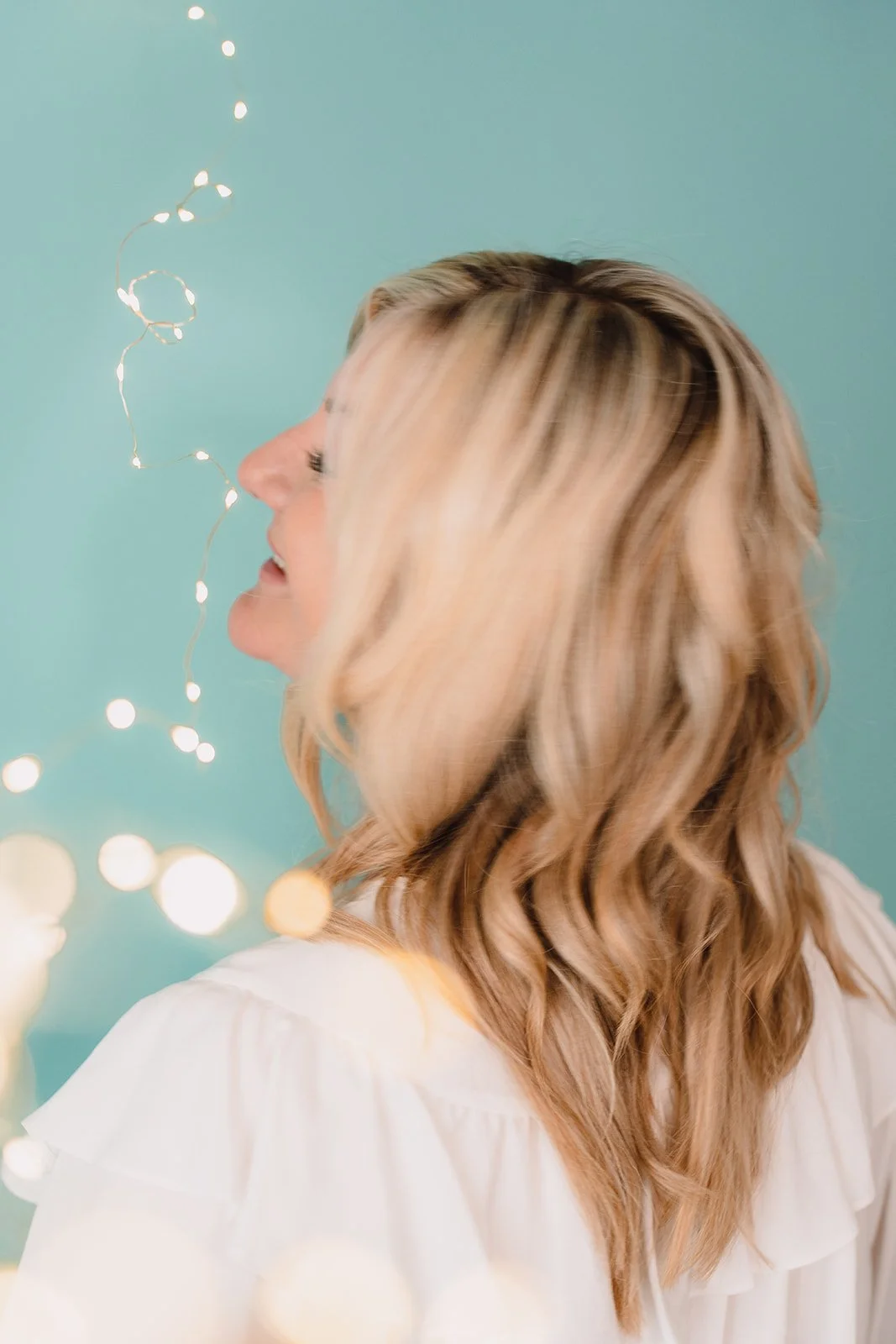 Profile portrait of Émilie Evans looking toward warm fairy lights, symbolizing reflection, inner light, and clarity in coaching.