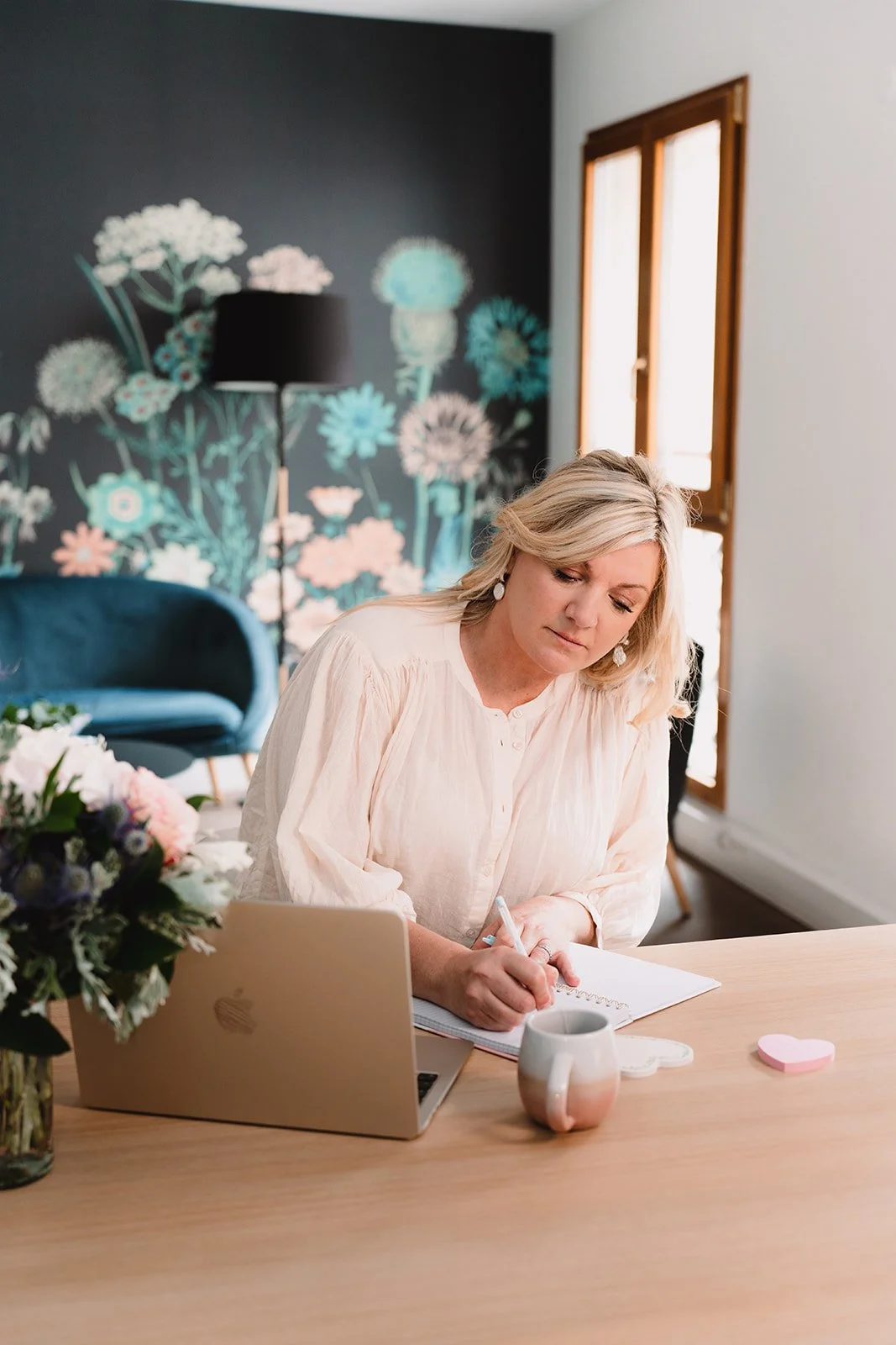 Émilie Evans sitting at her home office desk, writing in a notebook next to her laptop, symbolizing online consultation and planning.