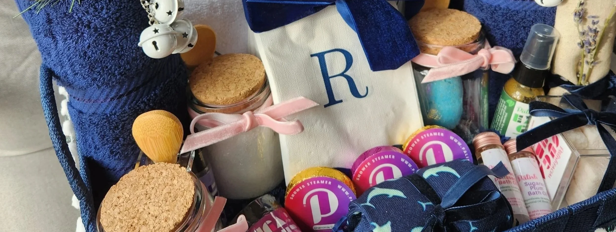 Gift boxes with assorted items including soaps, a towel, a hair clip, and snacks, decorated with colorful ribbons.