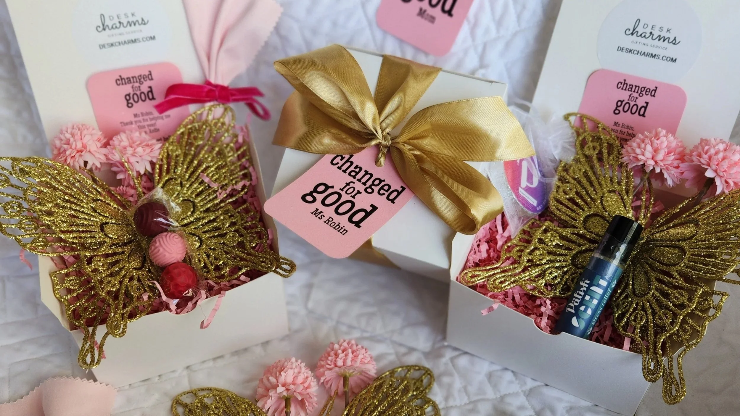 Gift boxes filled with various small items and treats, each tagged with a different label such as 'Coffee Lover,' 'Office Survival Kit,' 'You're a Big Dill,' 'Nurse,' 'Utterly,' and others, arranged on a table.
