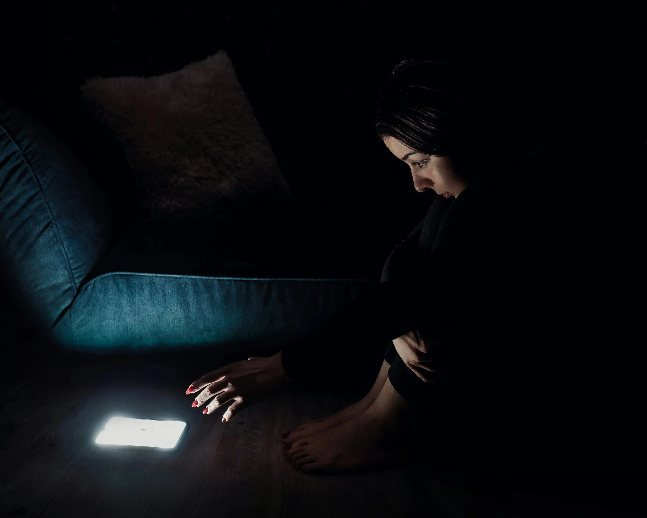 A young girl sitting in the dark looking at a bright phone screen