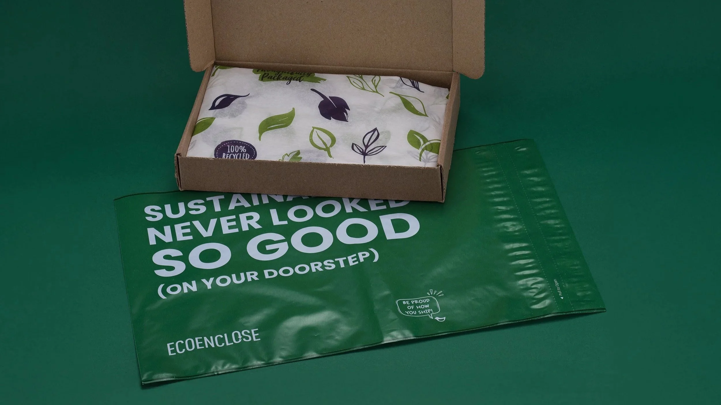 Eco-friendly packaging with a brown cardboard box and a green plastic bag that reads 'SUSTAINABLE NEVER LOOKED SO GOOD (ON YOUR DOORSTEP)'. The box contains tissue paper with green and purple leaf designs.