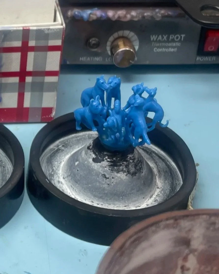 Small blue rubber or plastic figurines of various animals, including horses, placed on a hot melting plate in a kitchen or workshop setting.
