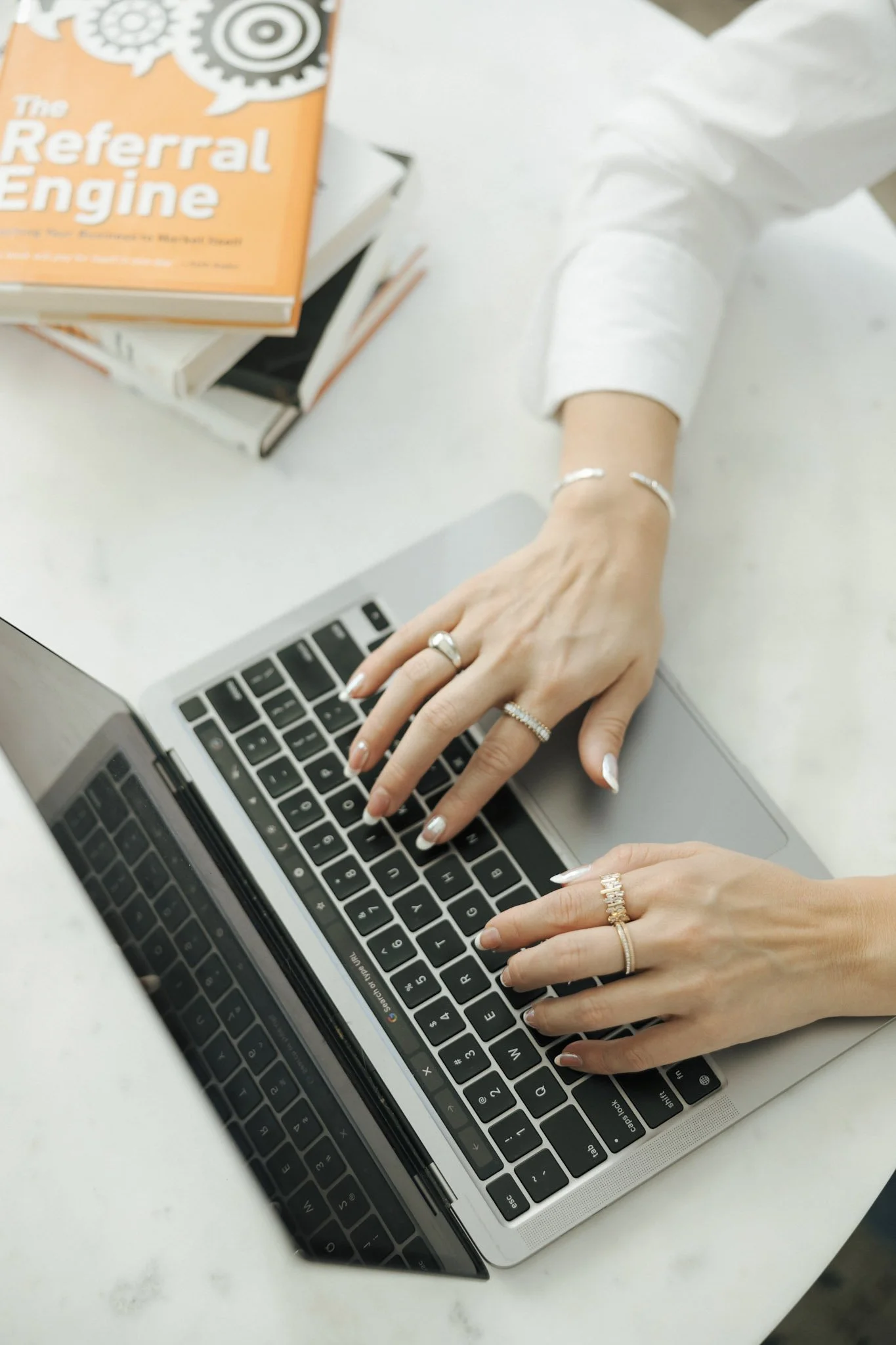 Person using a laptop at a white table with books about referral marketing.