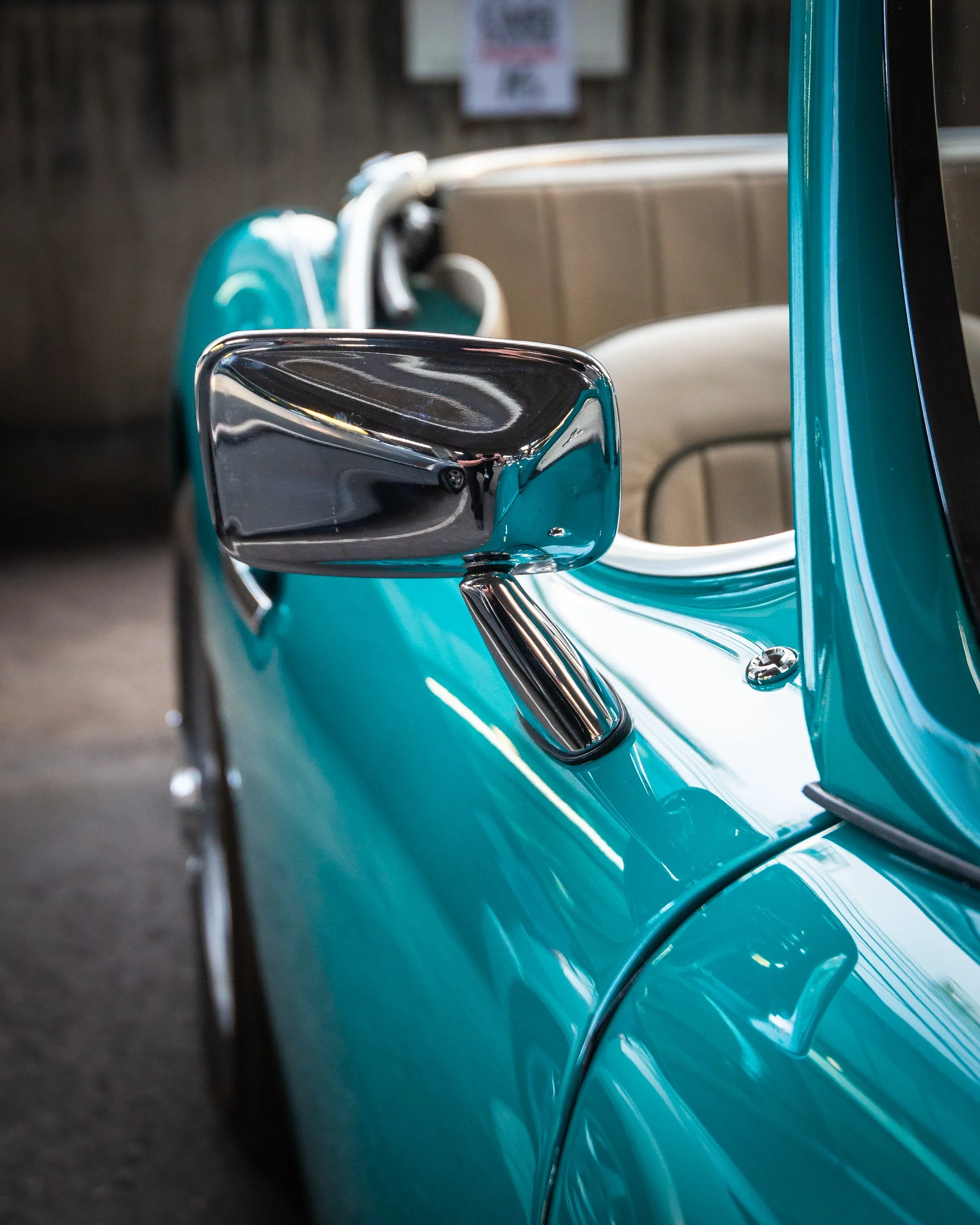 A close-up of a vintage turquoise car featuring a side mirror and part of the door, with a blurred background.