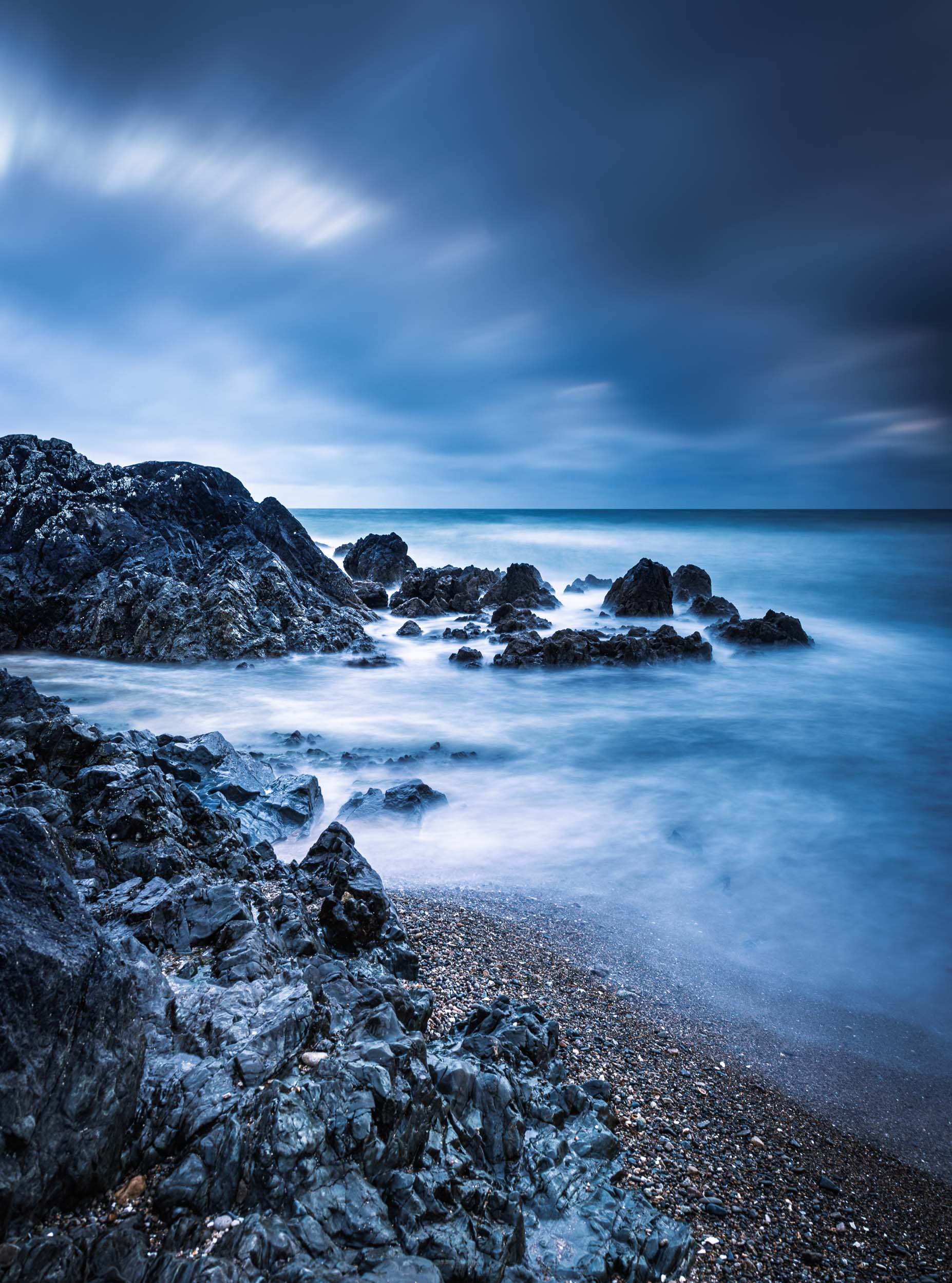 A long exposure photo of a rocky coastline with a cloudy sky and blurred ocean waves.
