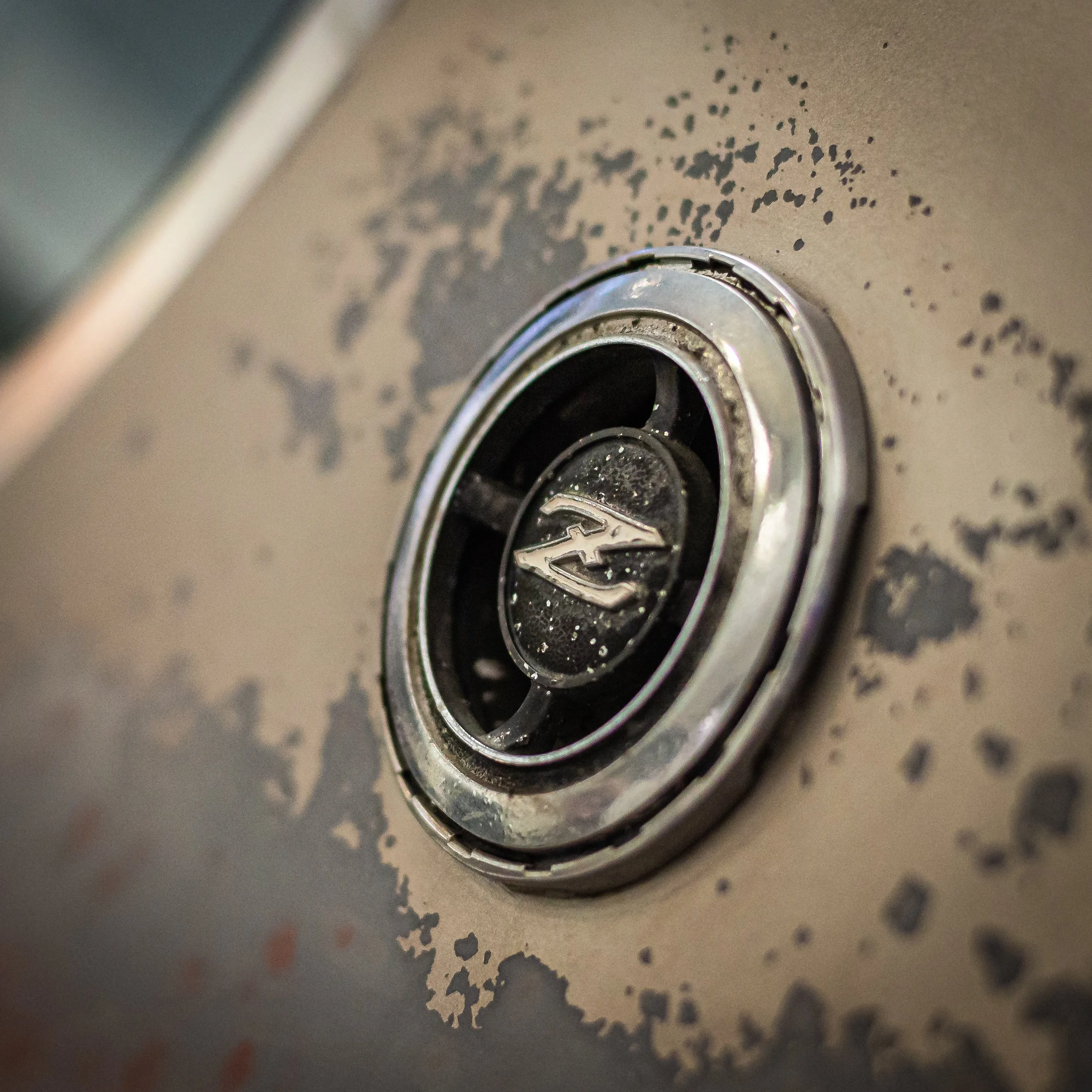 Close-up of a vintage Pontiac hubcap with rust and paint chipping on a beige surface.