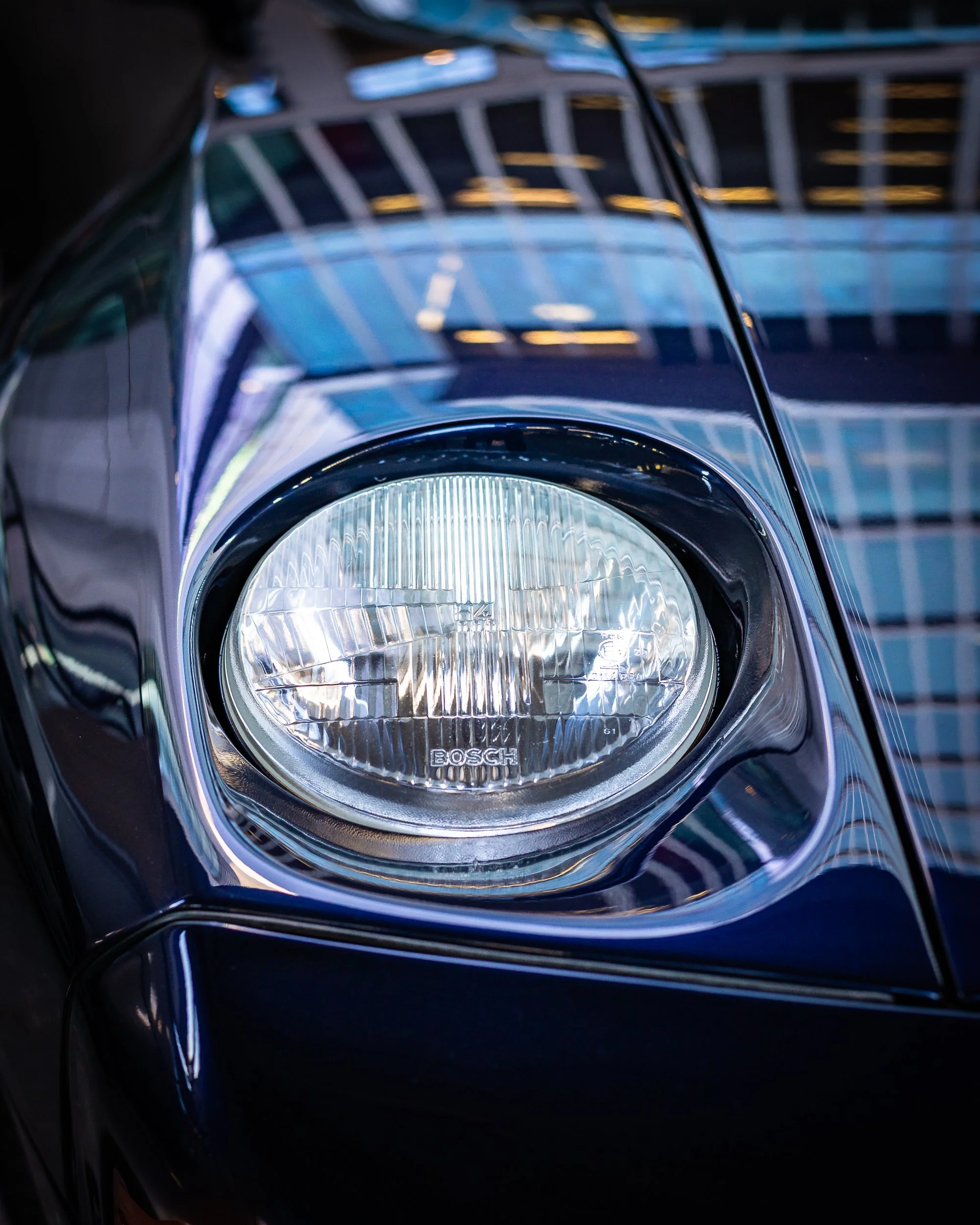 Close-up of the front headlight of a black car with a building reflected on its surface.