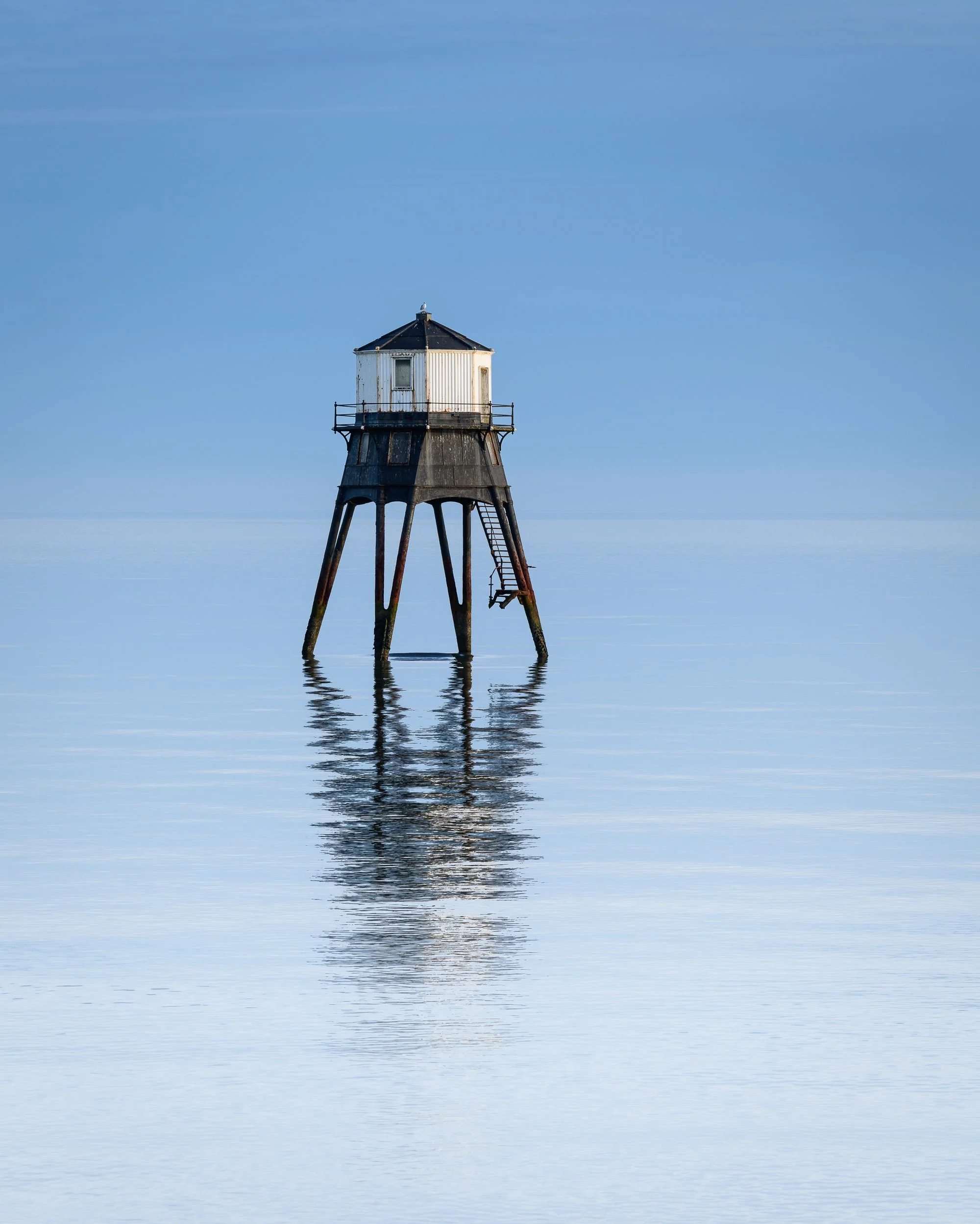 A lighthouse standing in calm water with a clear blue sky in the background.