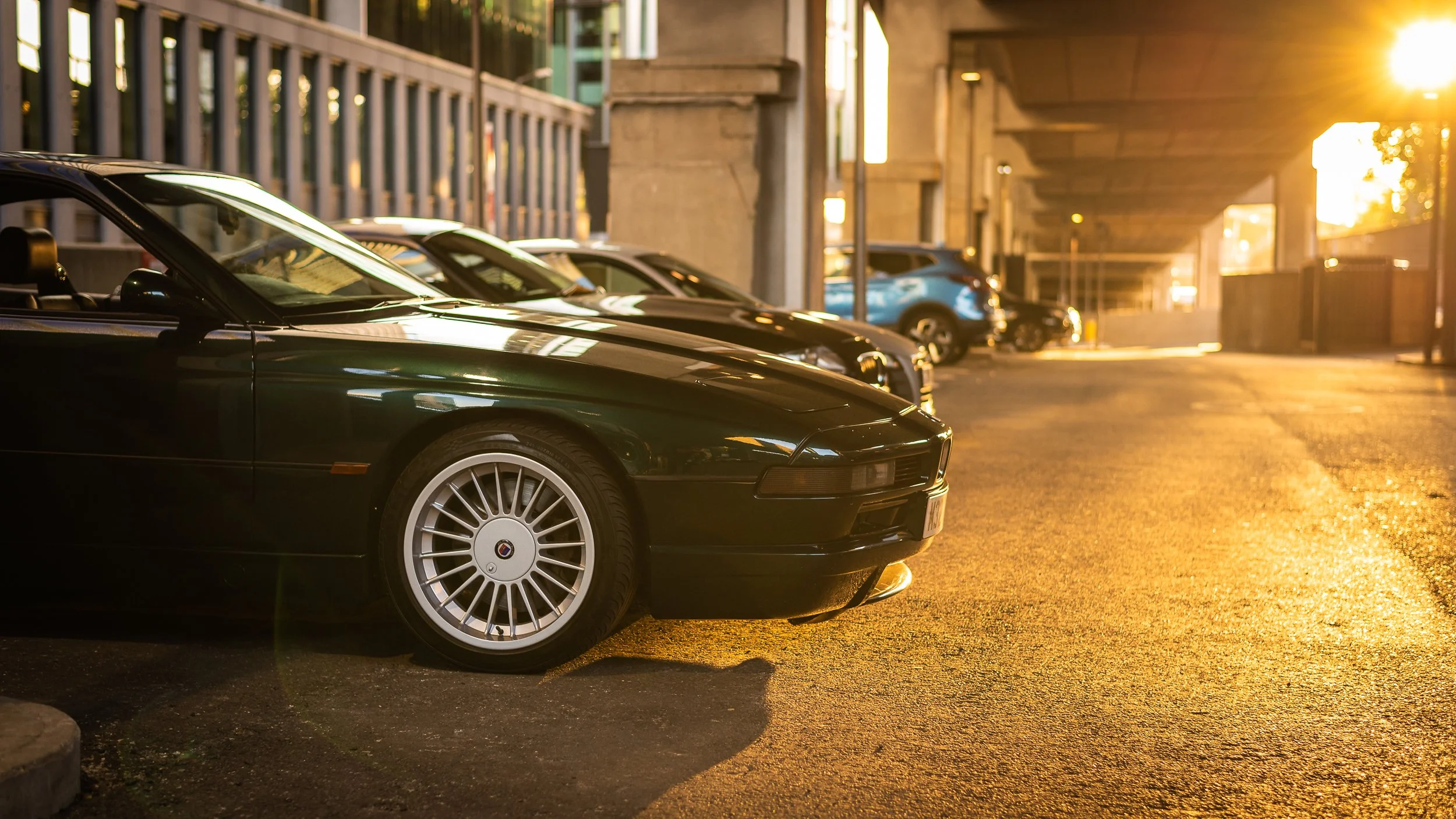 A row of parked cars under an overpass during sunset with warm golden lighting.
