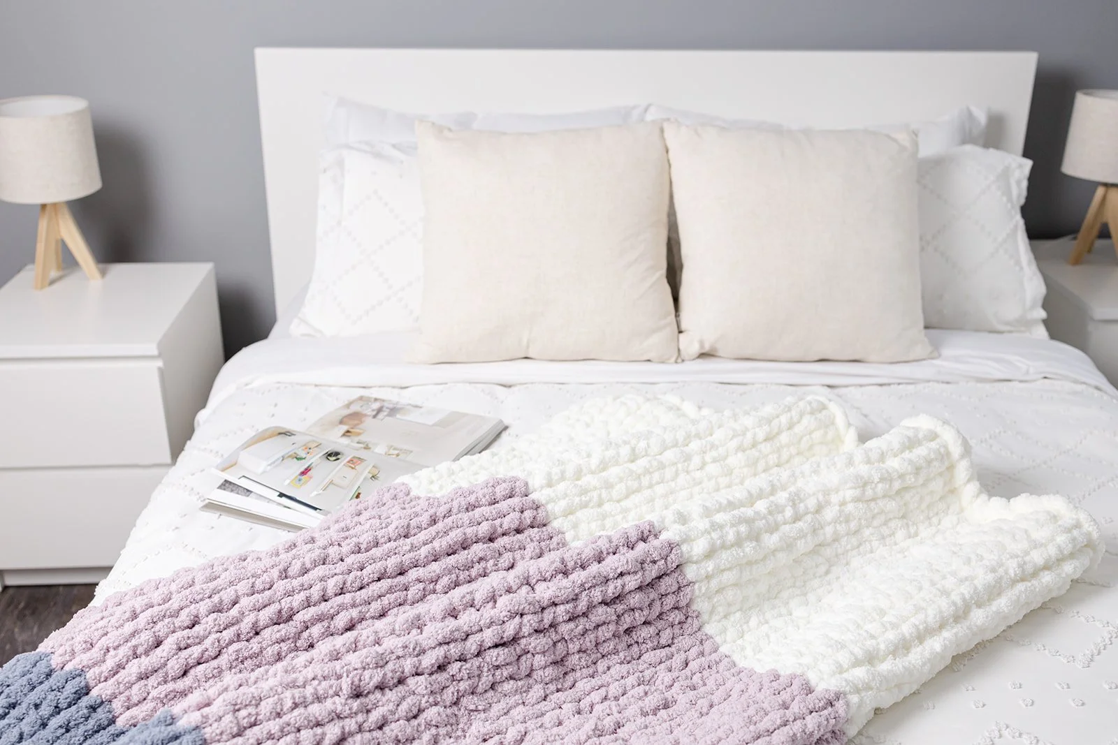 The Dini handmade chunky knit blanket in coastal blue, soft lavender & cream draped over a sofa