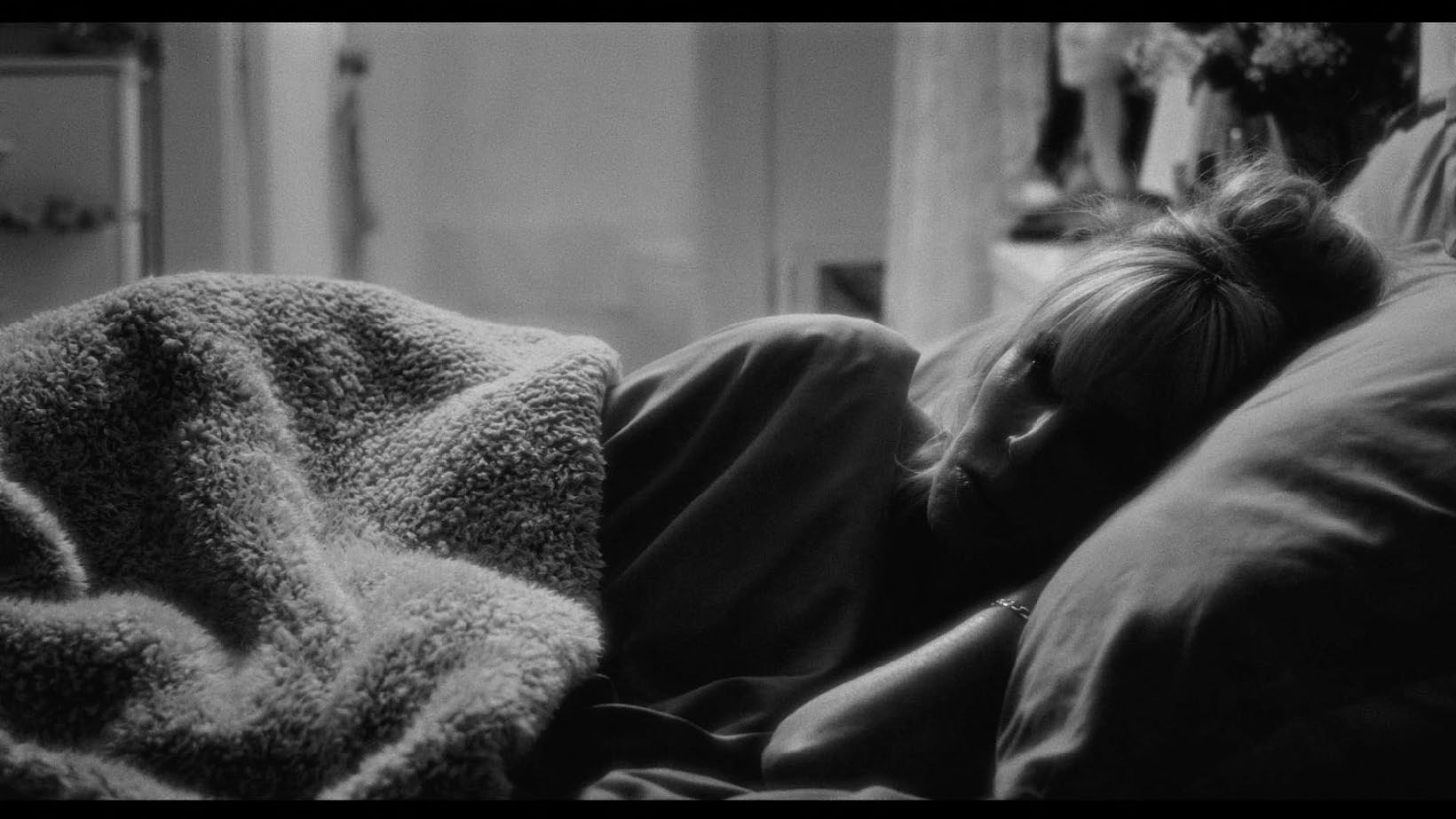 Black and white photo of a person lying in bed under a blanket.