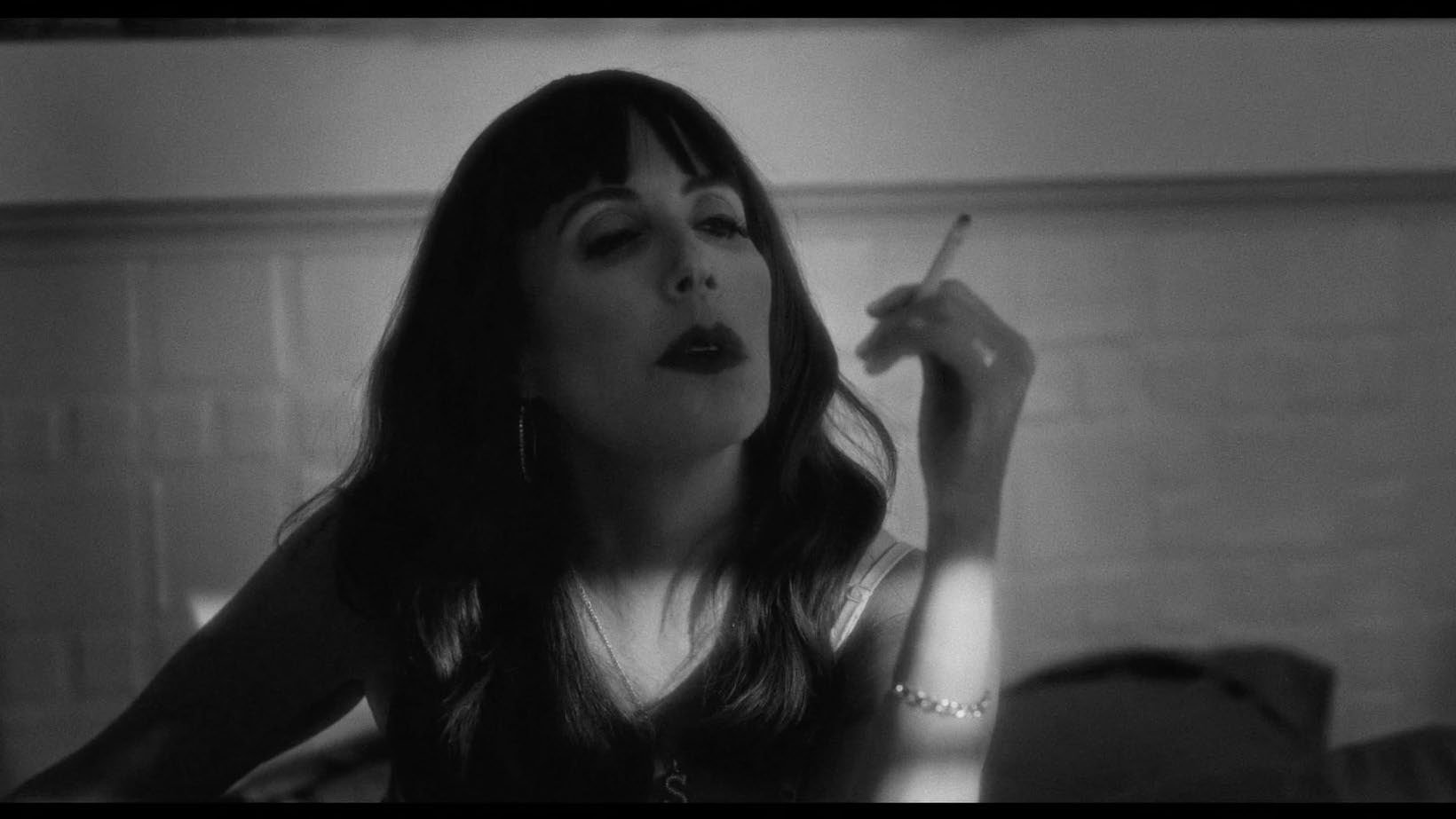 Black and white image of a woman smoking a cigarette indoors, looking contemplative.